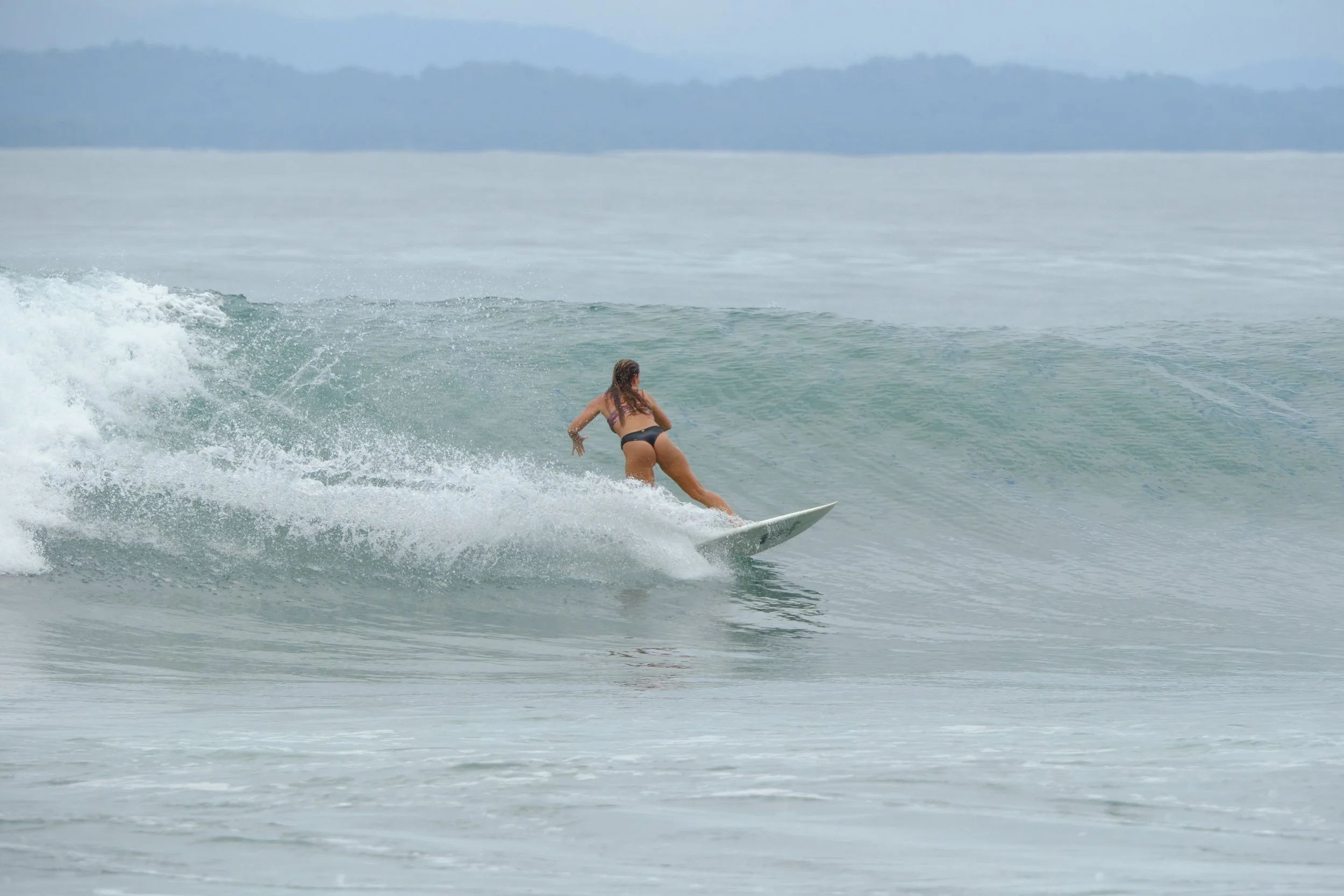 Woman surfing on a wave in the ocean during daytime, wearing a bikini.