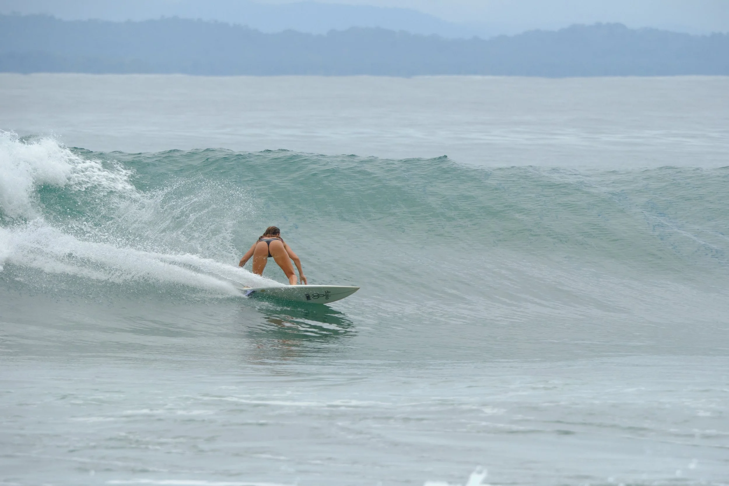 A woman in a black bikini surfing on a wave in the ocean during daytime.