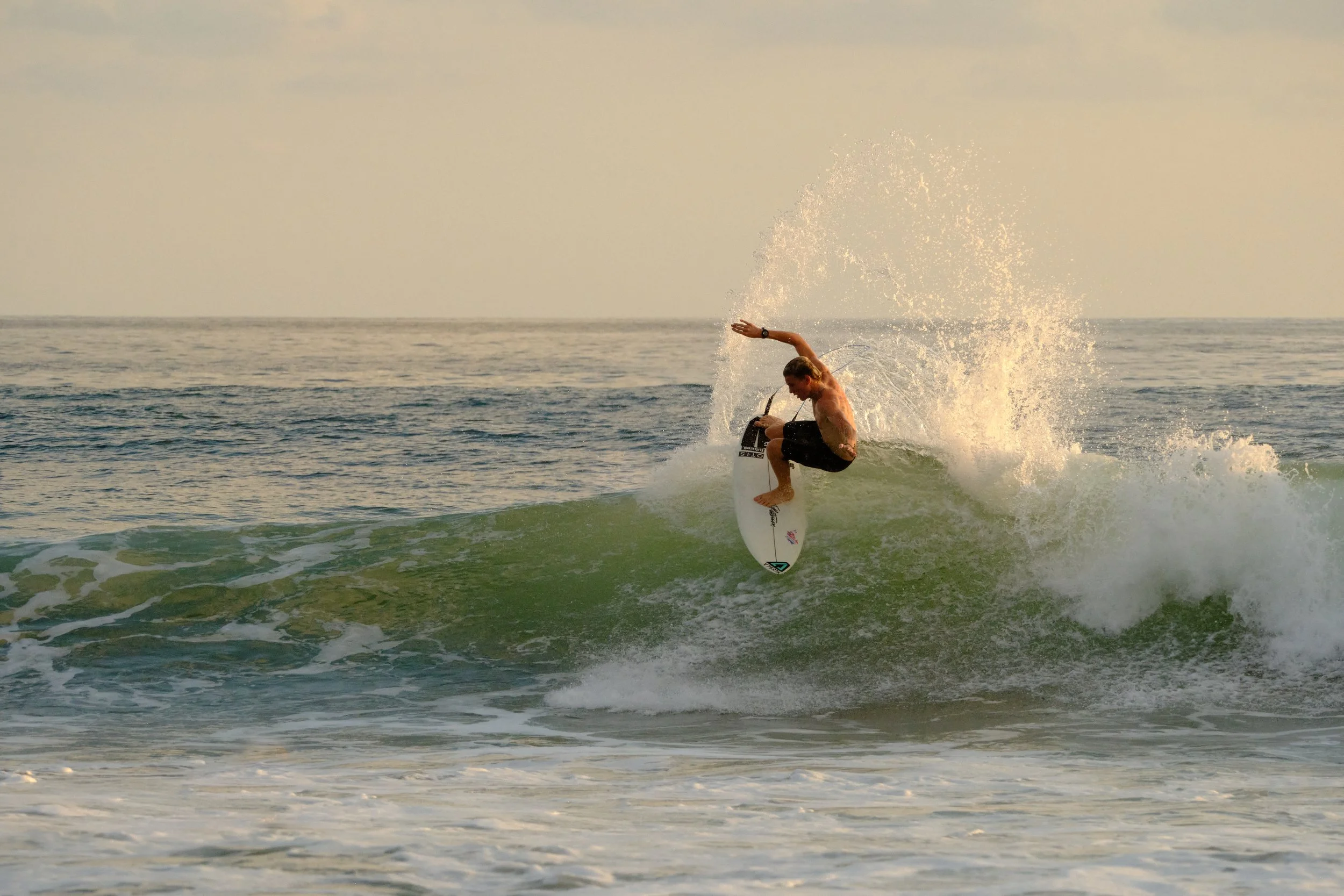 A man surfing on a wave in the ocean during sunset.