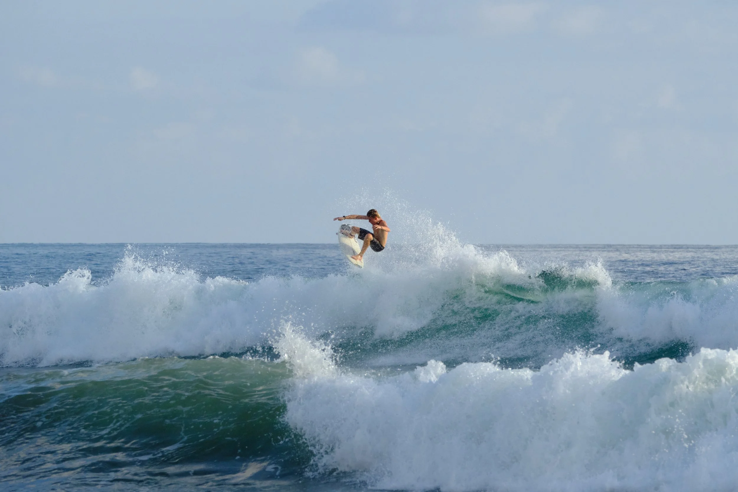 A surfer performing an aerial trick on a wave in the ocean during daytime.