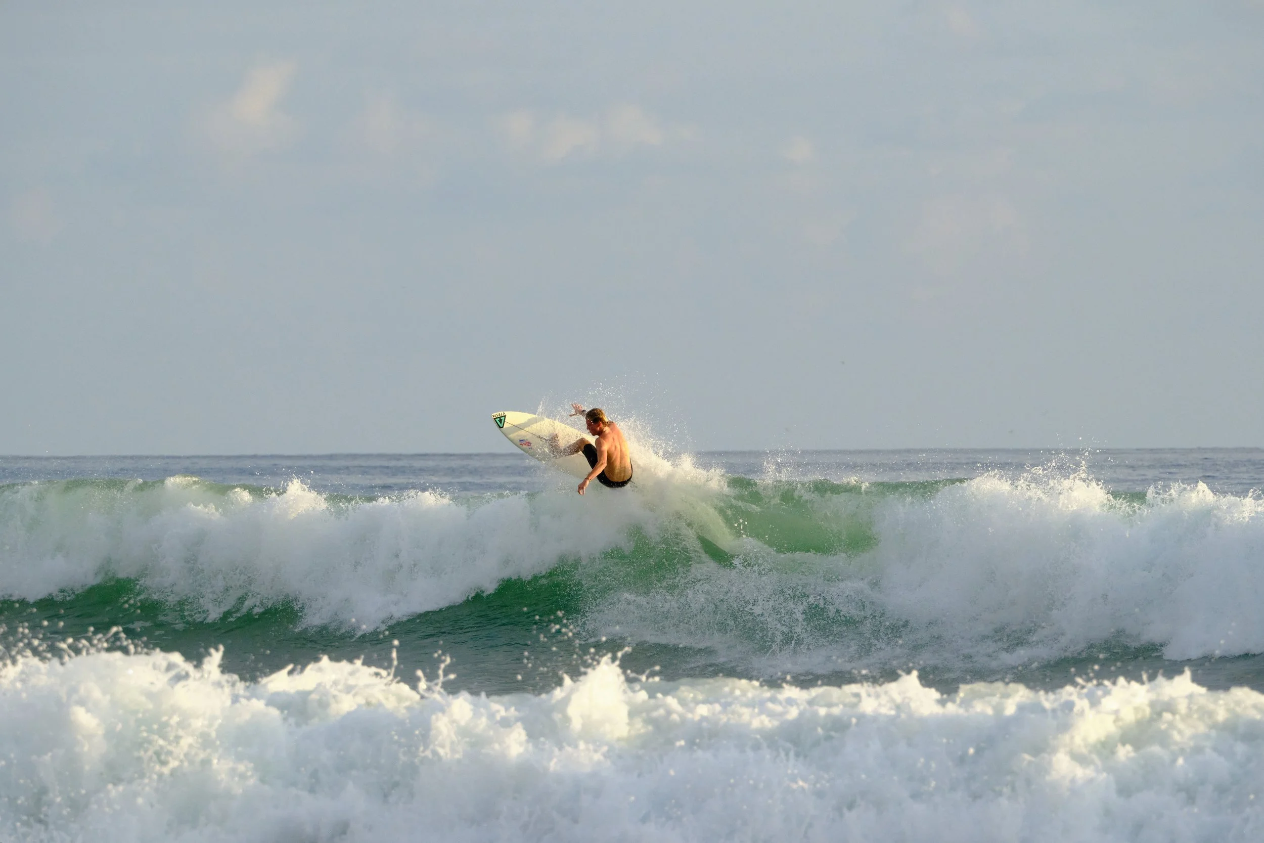 A shirtless man surfing on a wave at the beach during daytime.