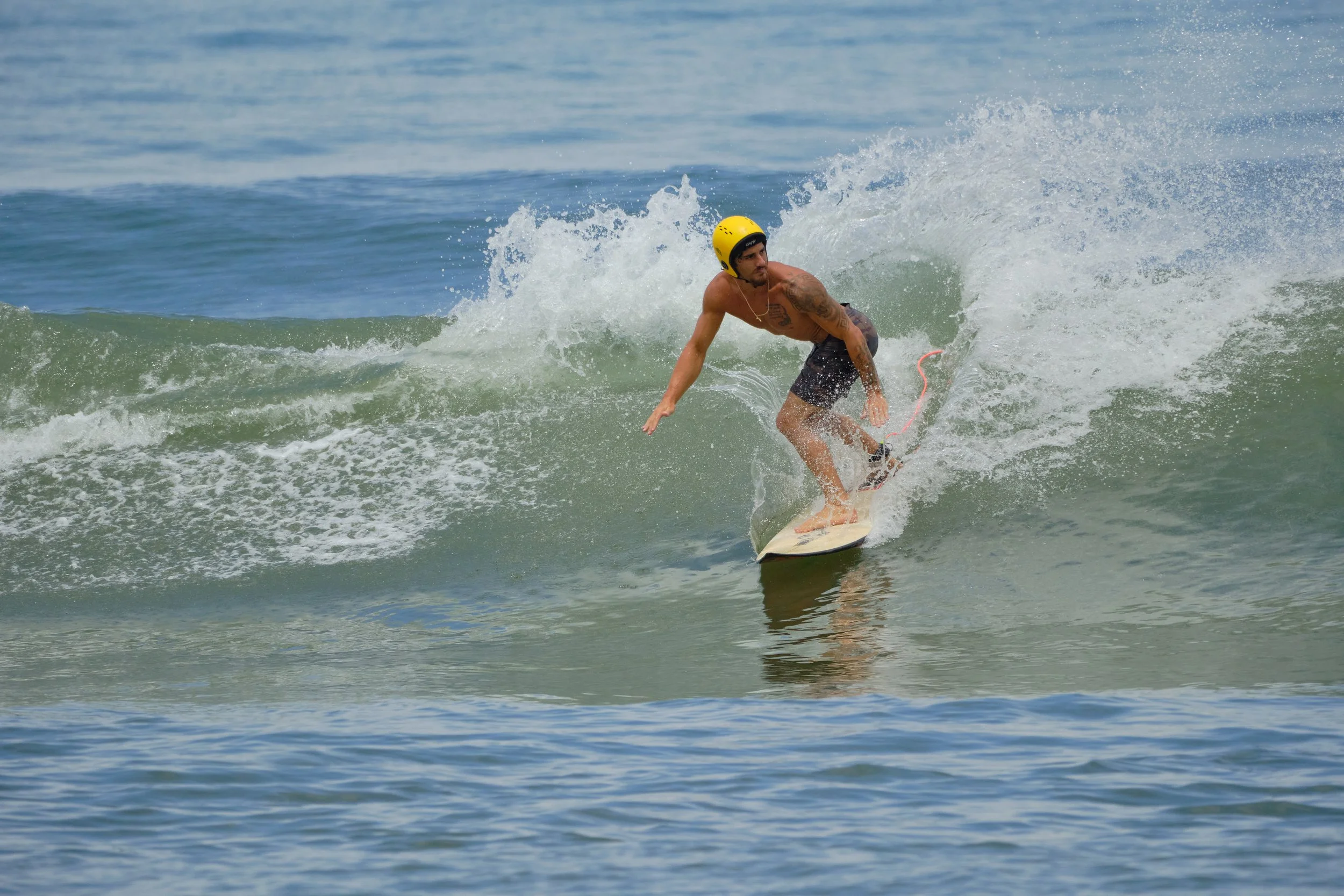 A man wearing a yellow helmet and black shorts surfing on a wave in the ocean.