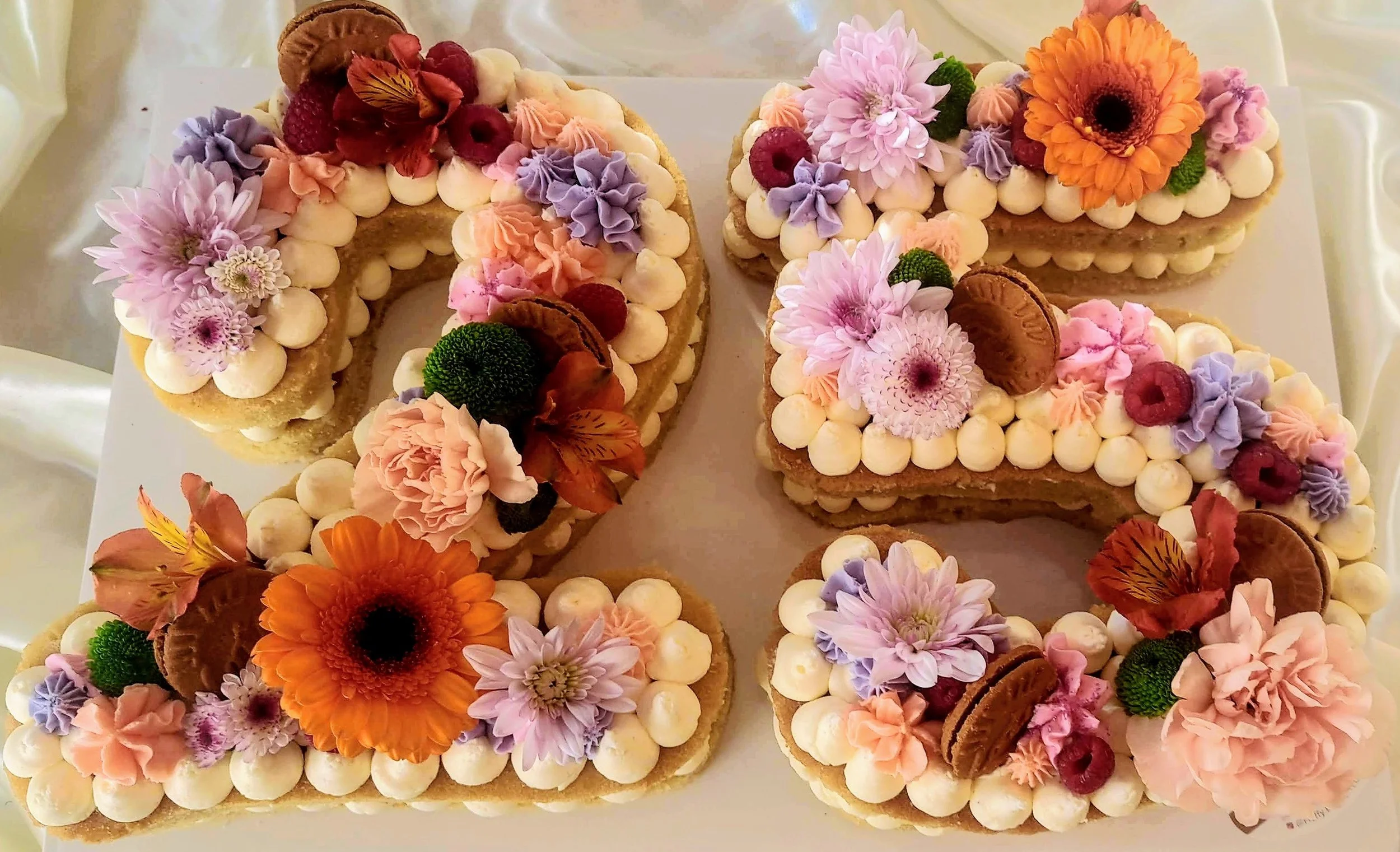 Decorated number-shaped cookies with flowers, macarons, berries, and frosting on white icing.