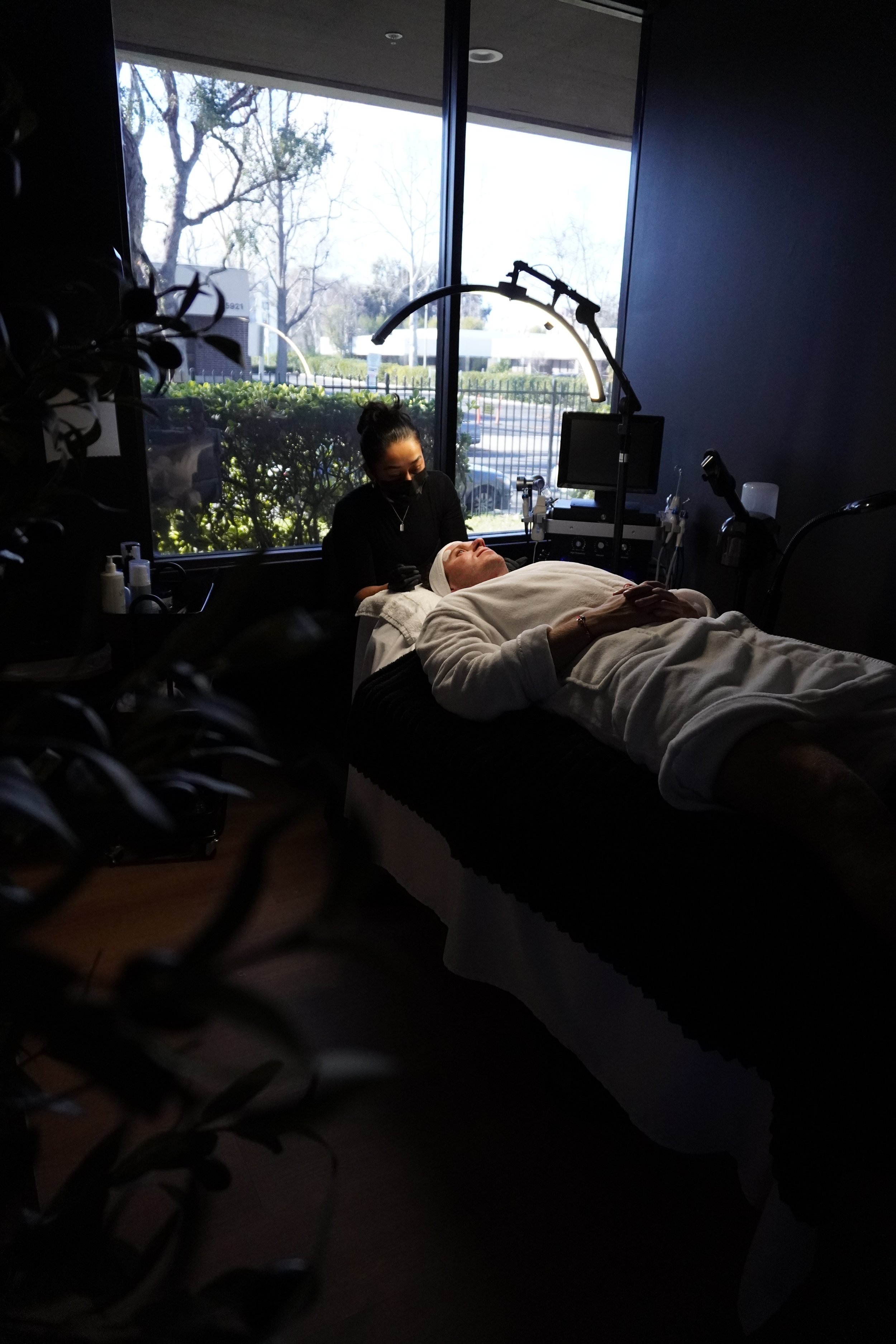 Skincare products including a brown dropper bottle, a white facial cleanser bottle, a white serum bottle, a small jar, and a silver tray on a black surface with a rolled towel.