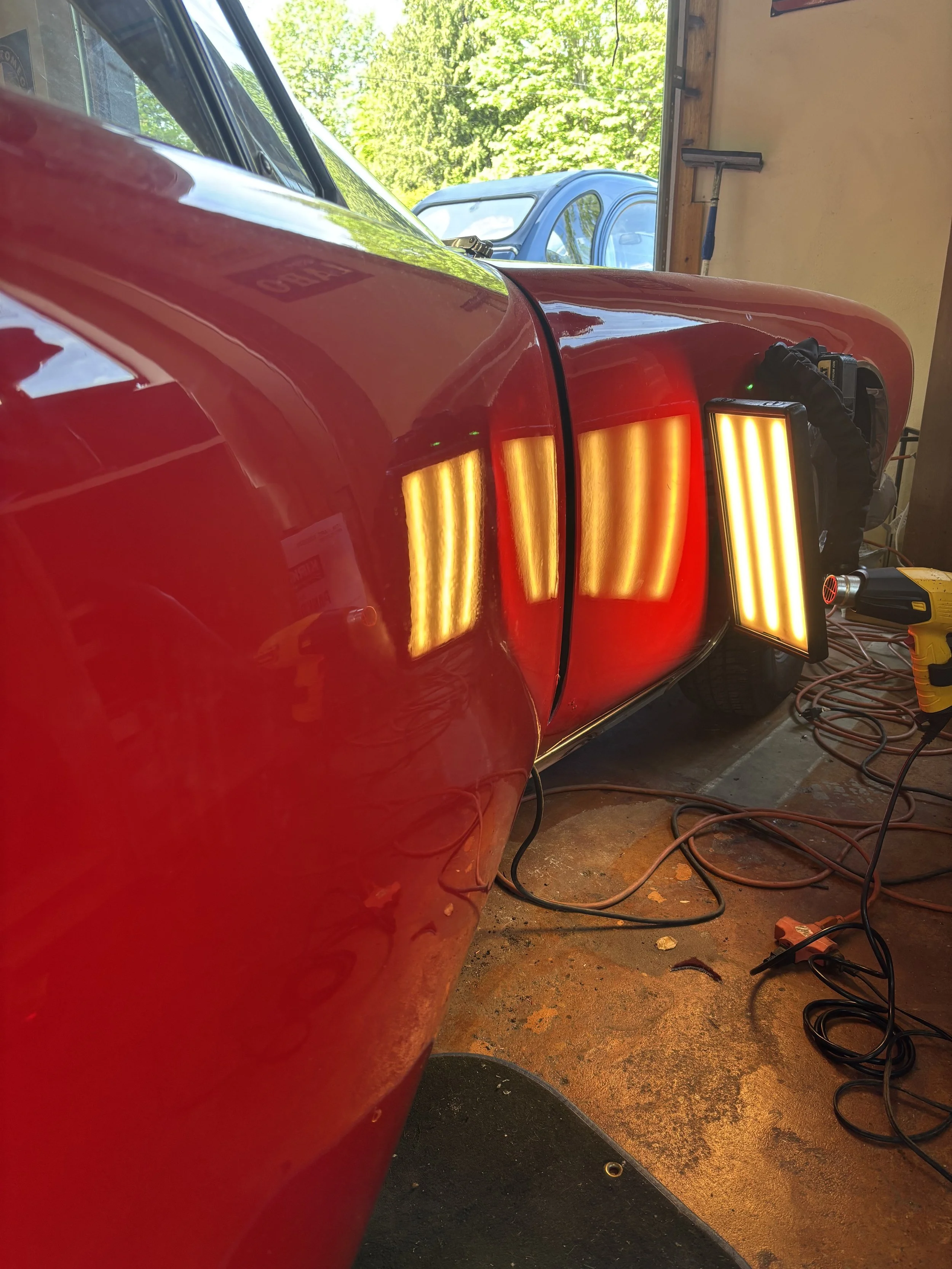 Red vehicle with reflection stripes in a garage, showcasing dent repair equipment and cables.