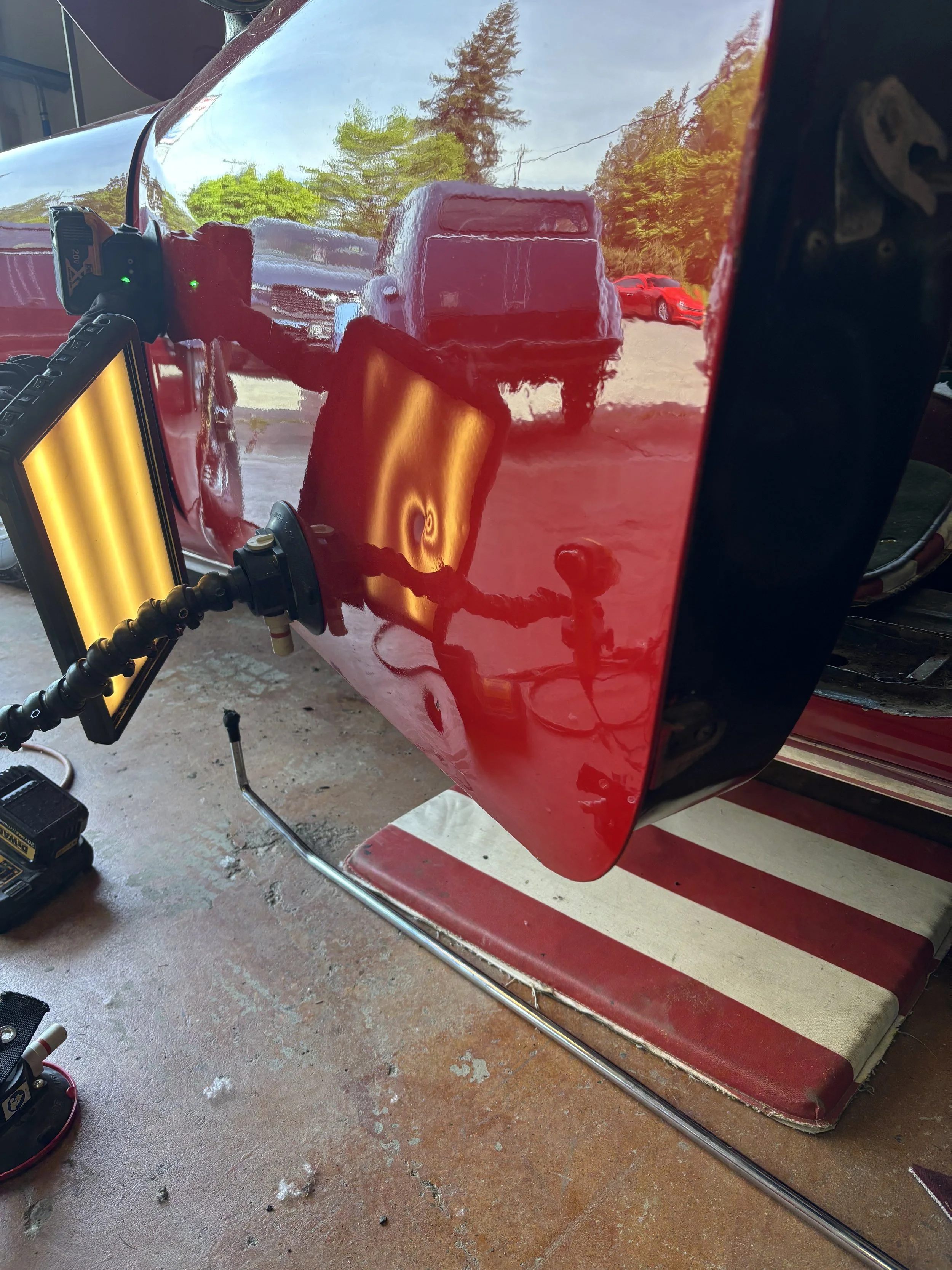 Car door dent repair using PDR lights and tools, with reflections of trees and vehicles on the surface.