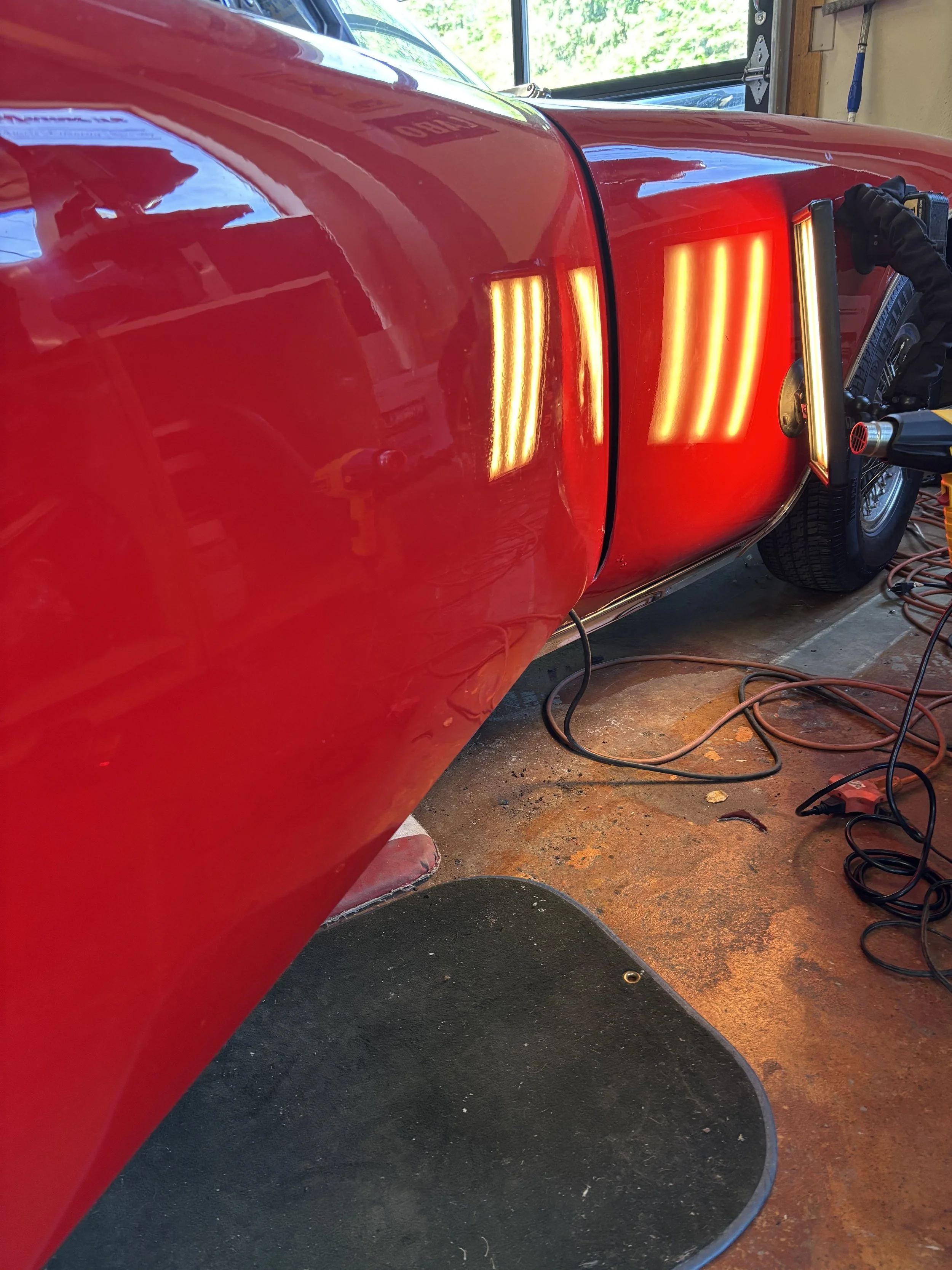 Close-up of red classic car paintwork being polished in a garage