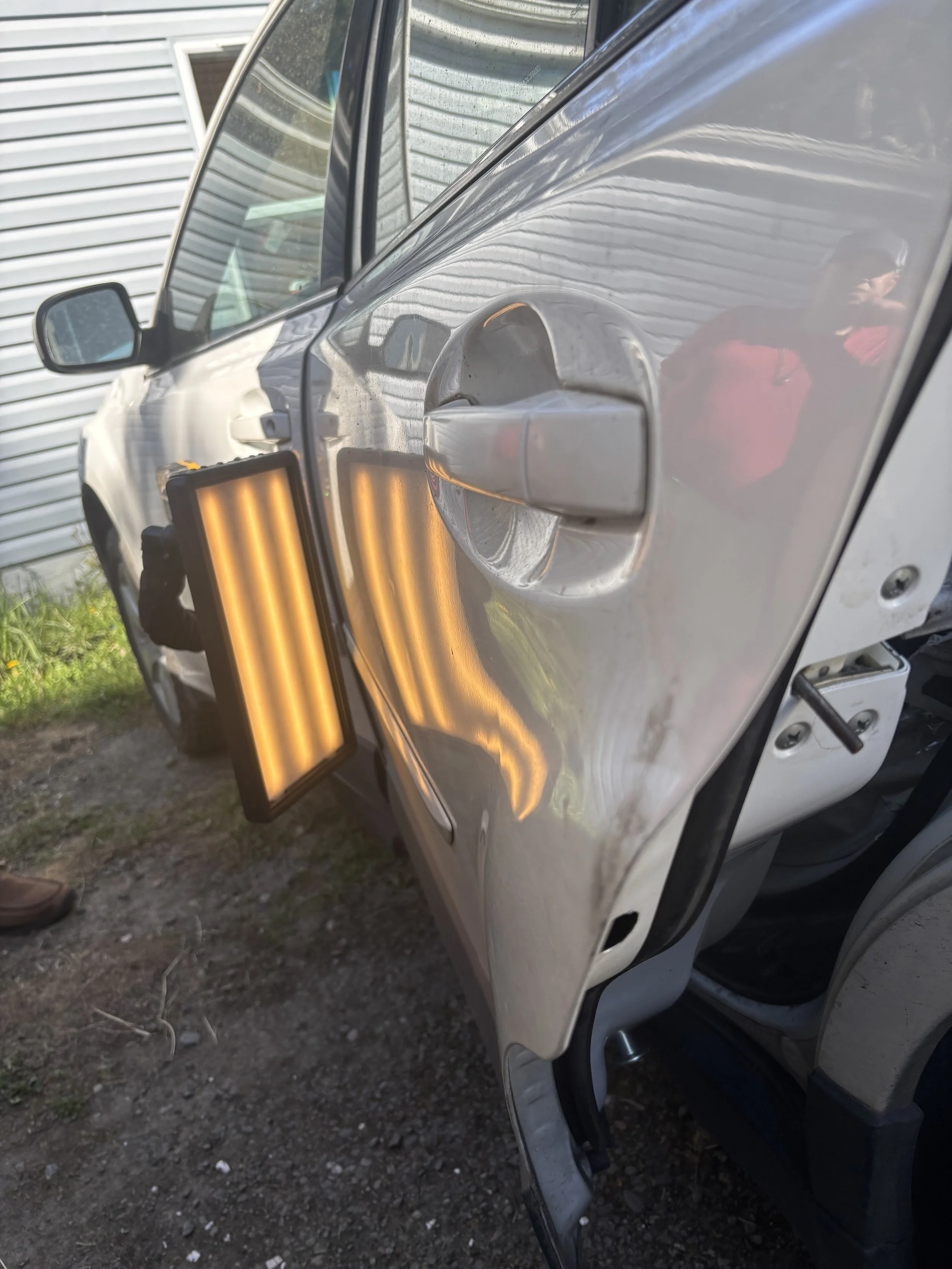 Close-up of a car door with a dent repair light reflecting on the surface, showing the car's damaged side panel.