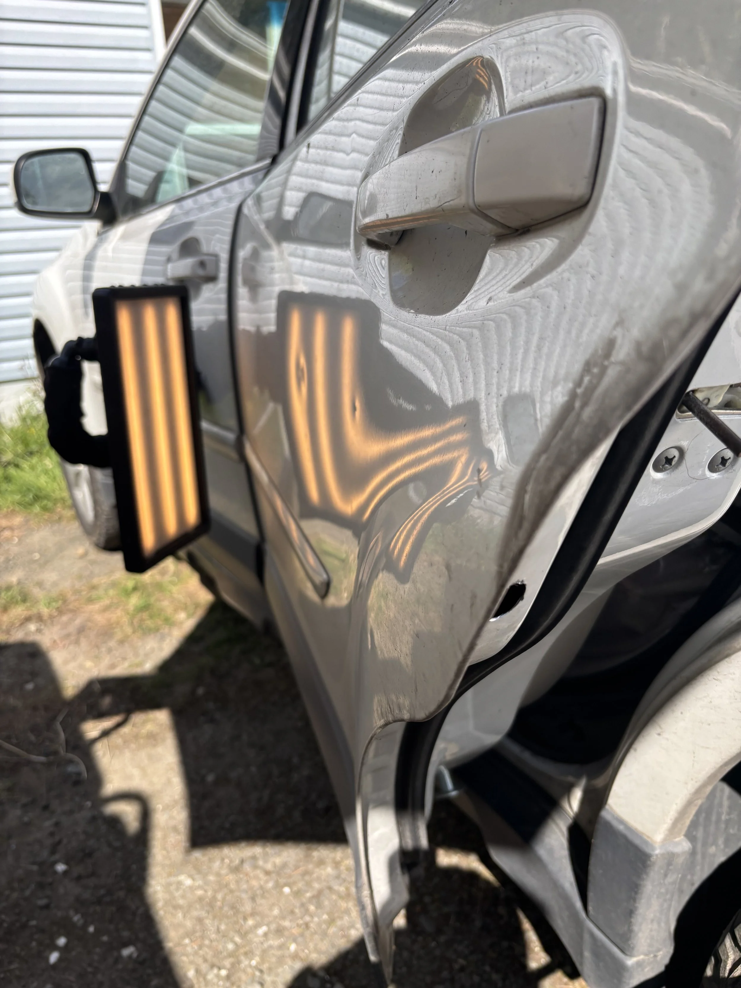 Car with a paintless dent repair tool reflecting light on the door to show dents.