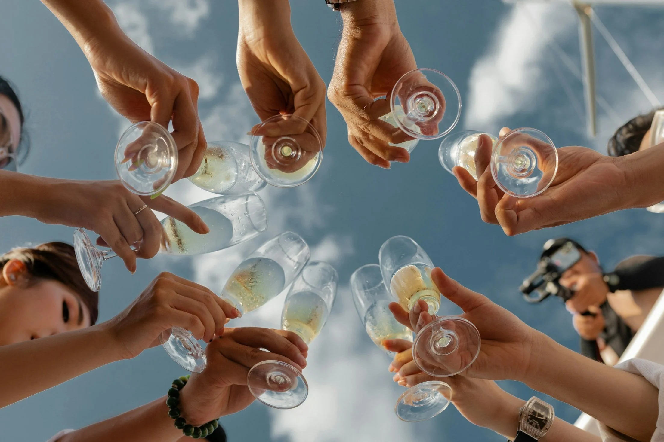 Group of people raising champagne glasses in a toast against a blue sky.