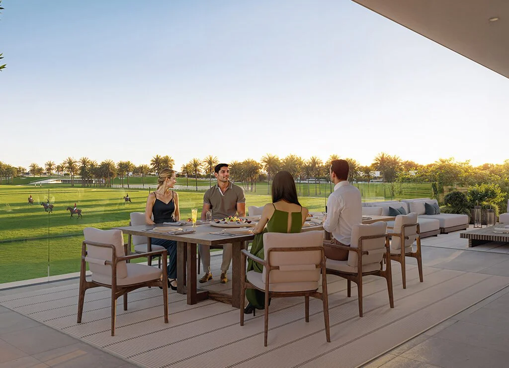People dining on a terrace overlooking a golf course with palm trees at sunset.