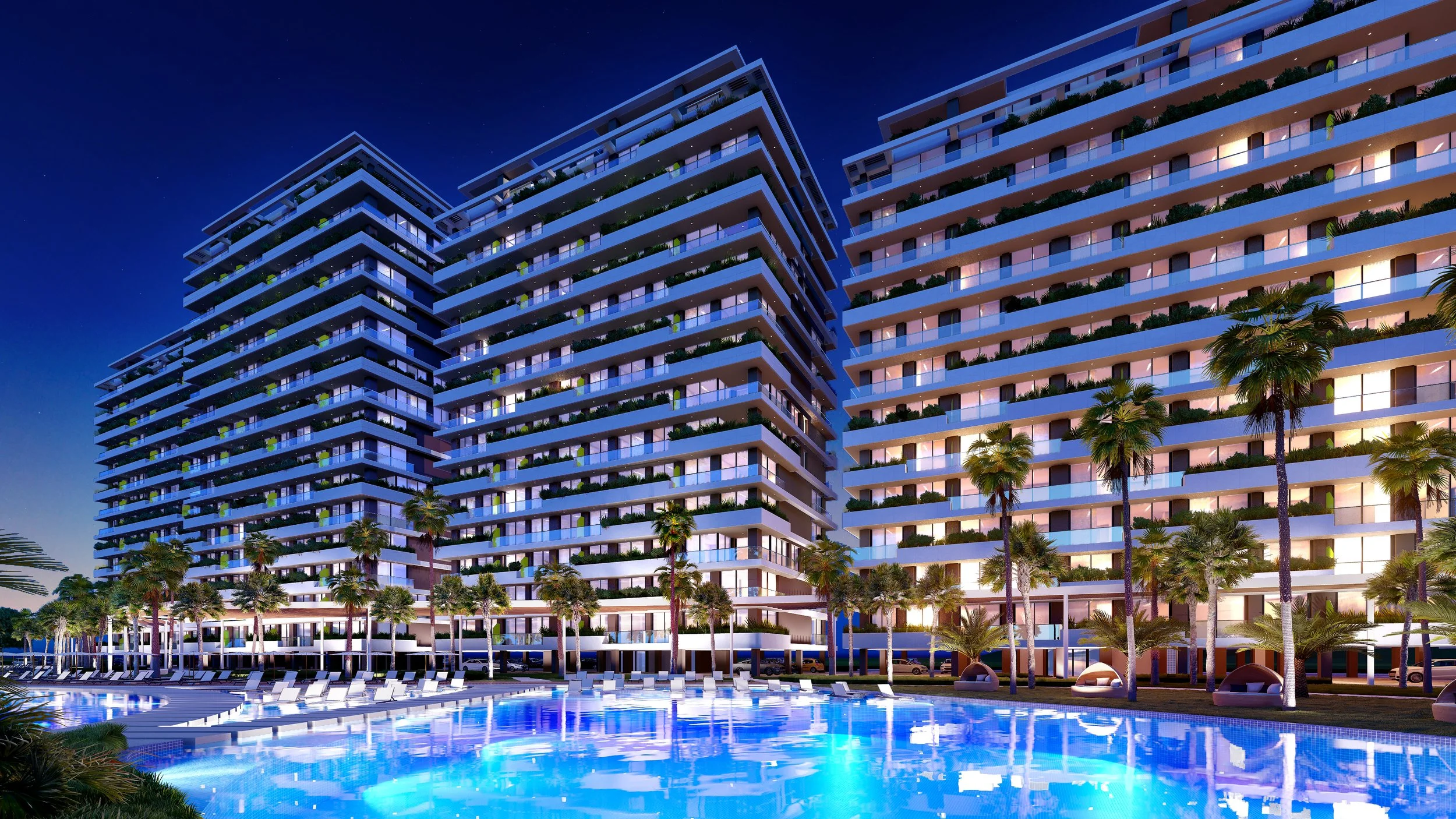 Night view of a modern residential complex with lit balconies, surrounded by palm trees, and a large illuminated swimming pool in the foreground.