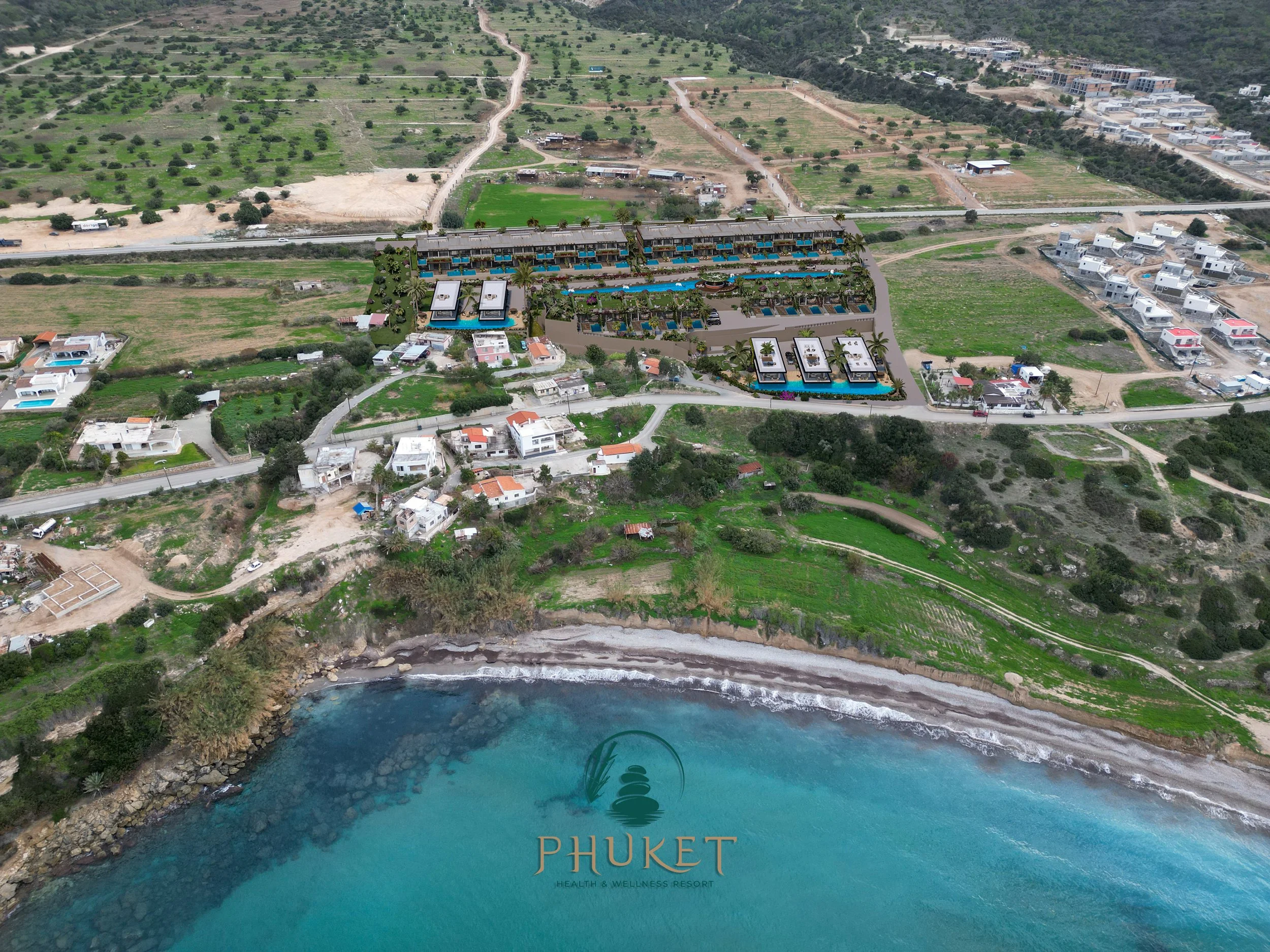 Aerial view of Phuket Health & Wellness Resort located on the coast with a beach, turquoise water, and lush green landscape, featuring modern resort buildings with pools, surrounded by residential houses and farmland.