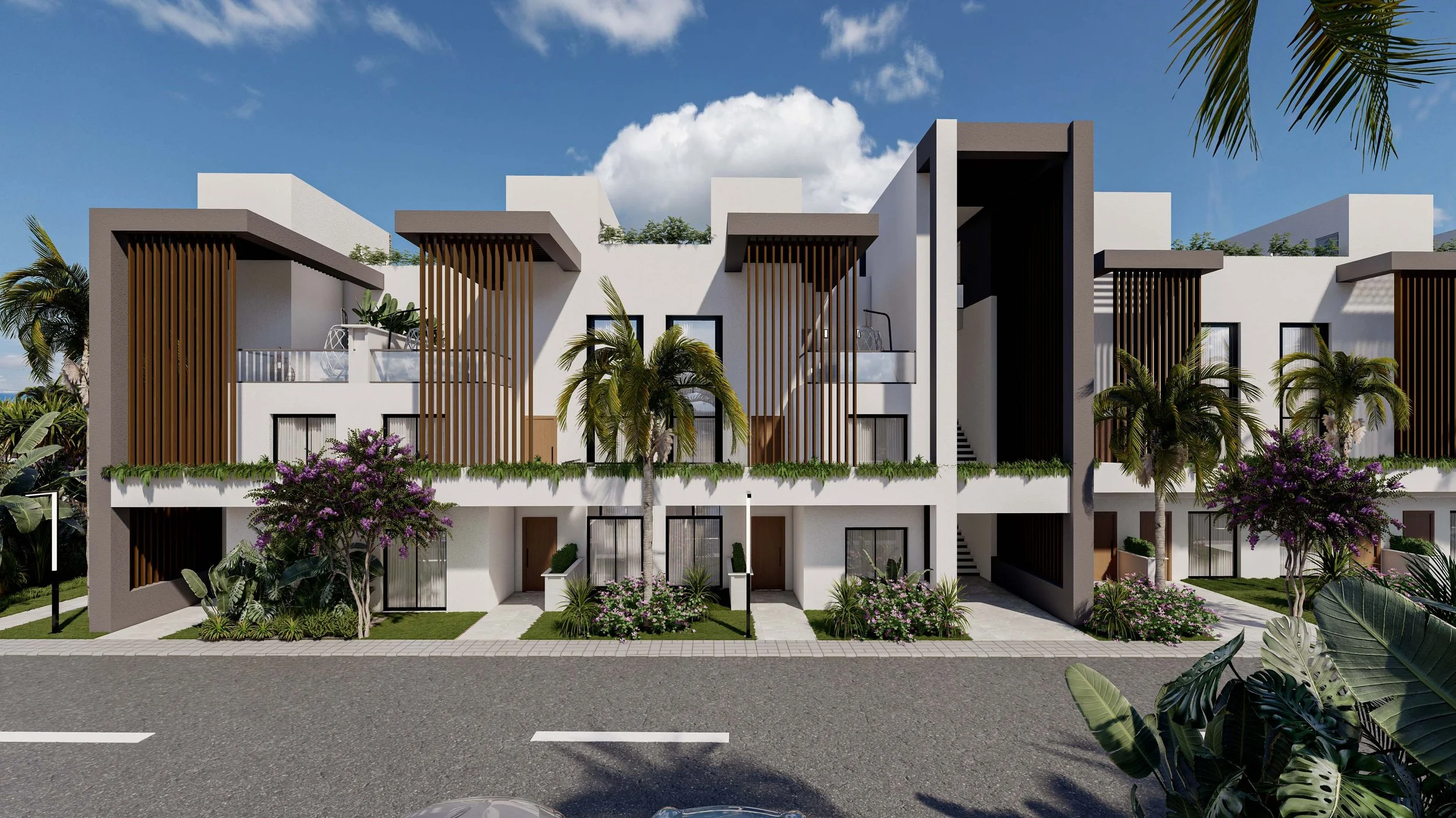 Modern multi-story residential building with white walls, brown wooden accents, balconies, and tropical landscaping including palm trees and flowering bushes, under a blue sky with clouds.