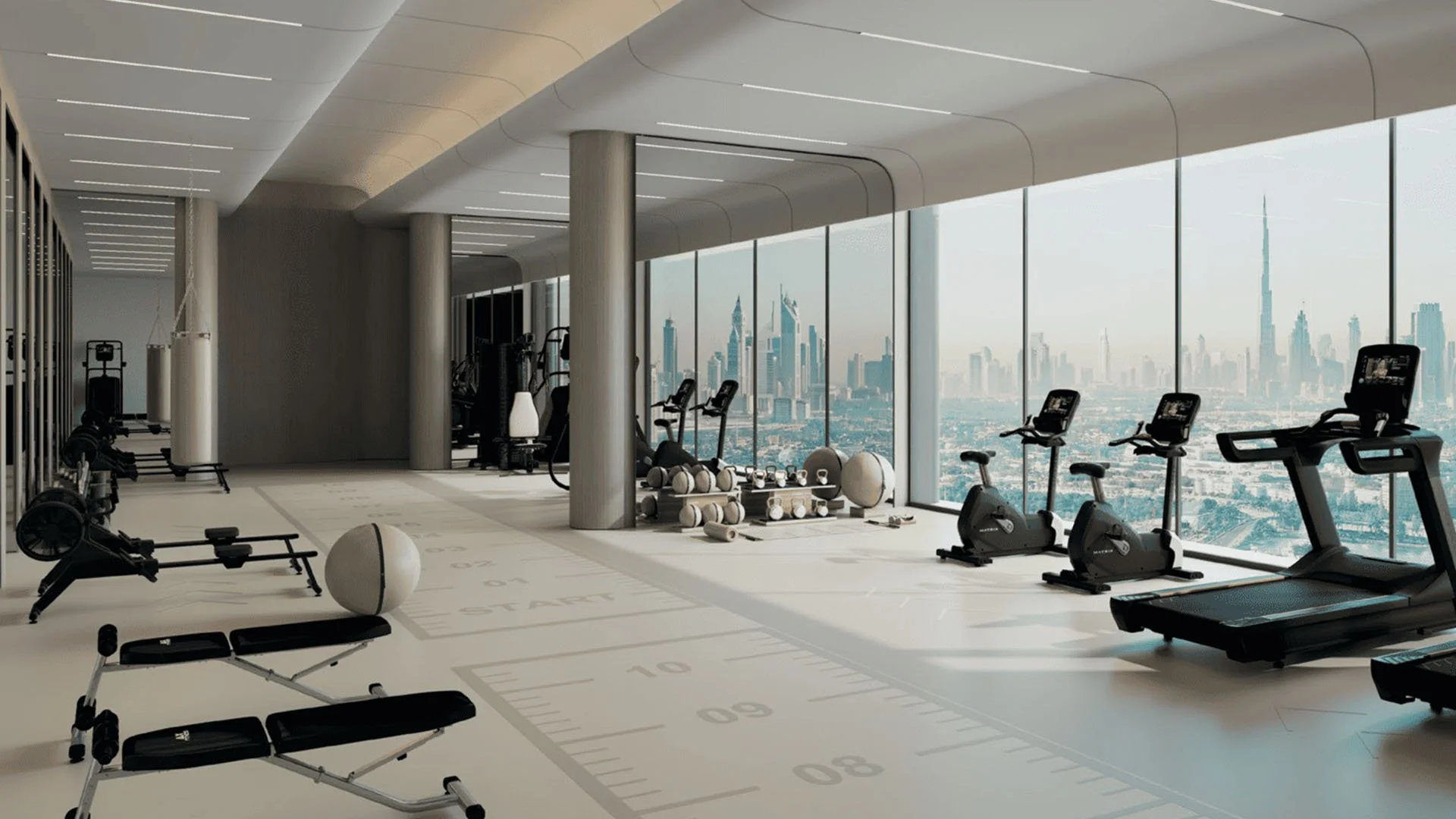 Modern gym with exercise equipment including treadmills, stationary bikes, weight machines, and free weights, in a high-rise building with large windows overlooking a city skyline.