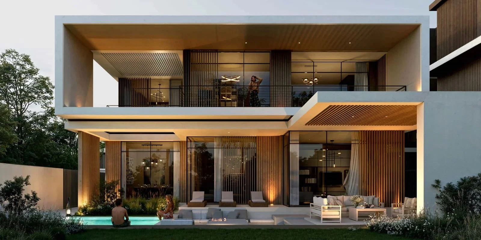Modern three-story house with large balconies, outdoor seating area, and illuminated pool with two people sitting nearby at sunset.