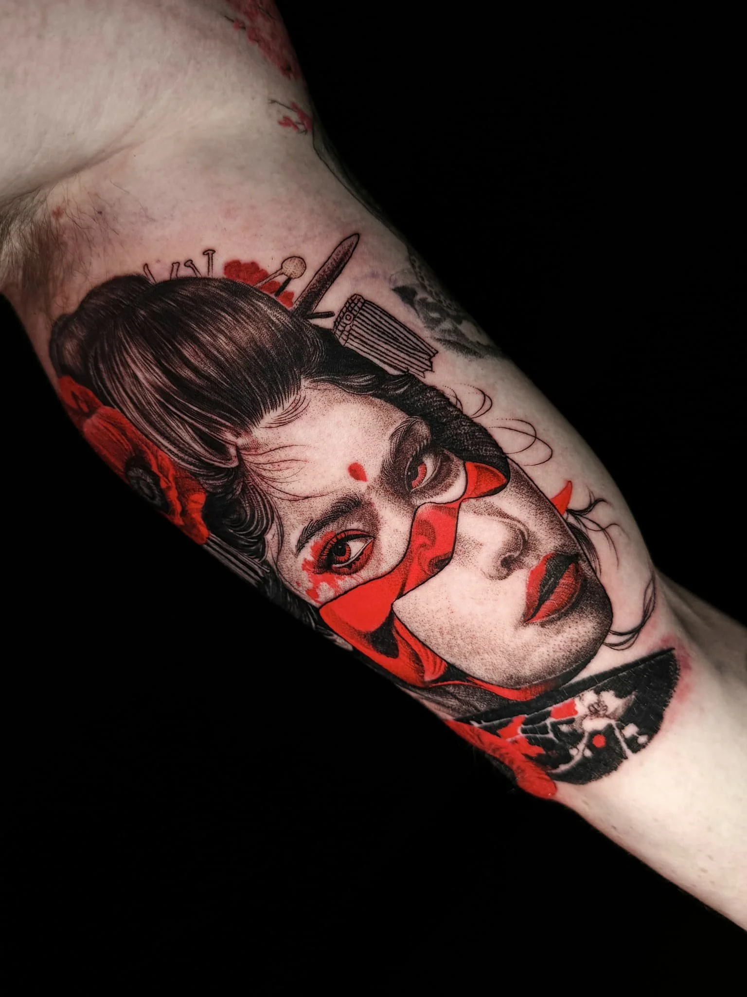 Black and gray tattoo of a woman's face with red accents, featuring traditional Japanese styling and a hair ornament.