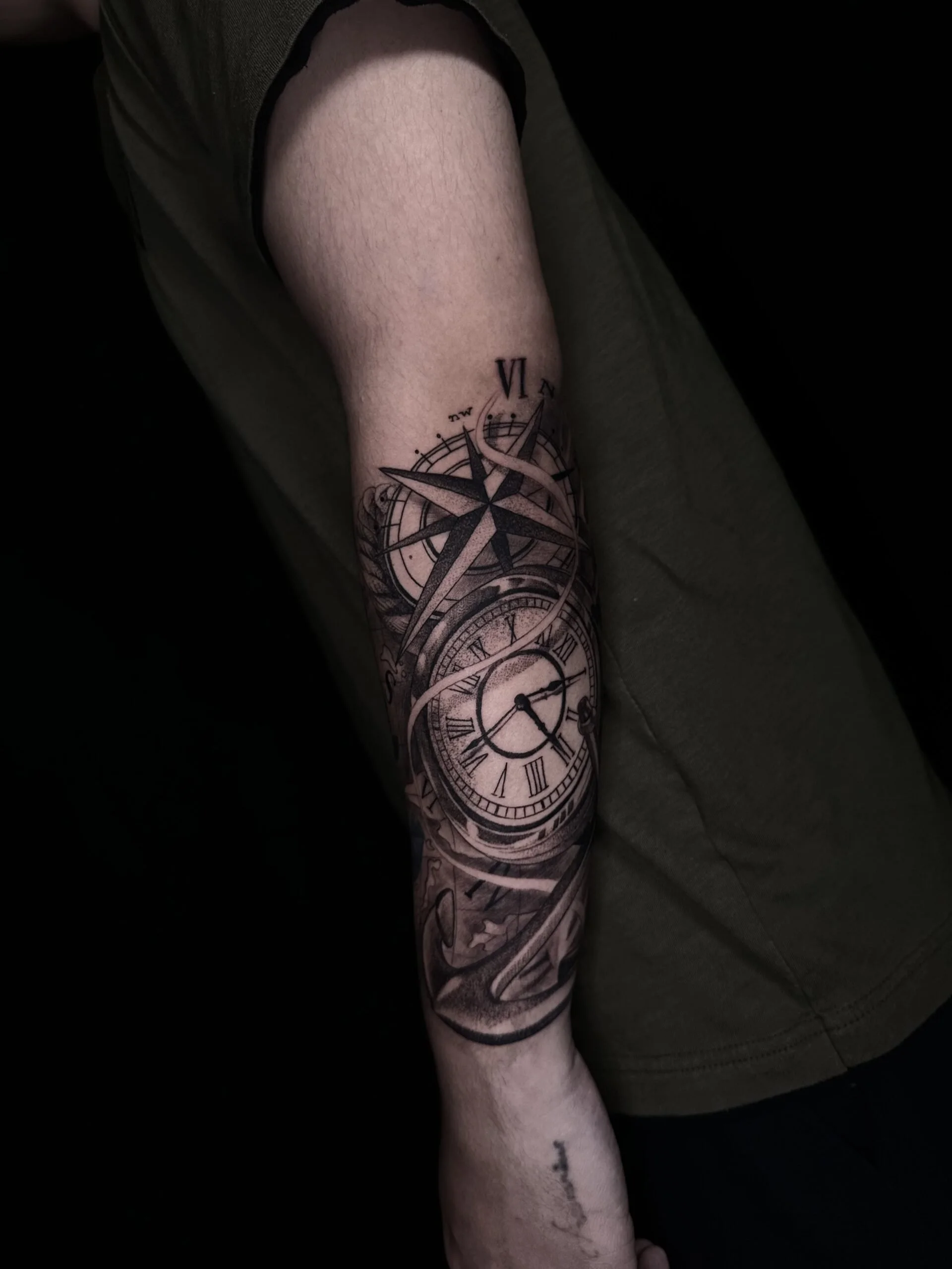 Tattoo of a vintage clock with Roman numerals, a compass rose, and swirling decorative elements on a person's forearm.