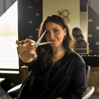 A young woman with long dark hair holding a pair of scissors in front of her, smiling.