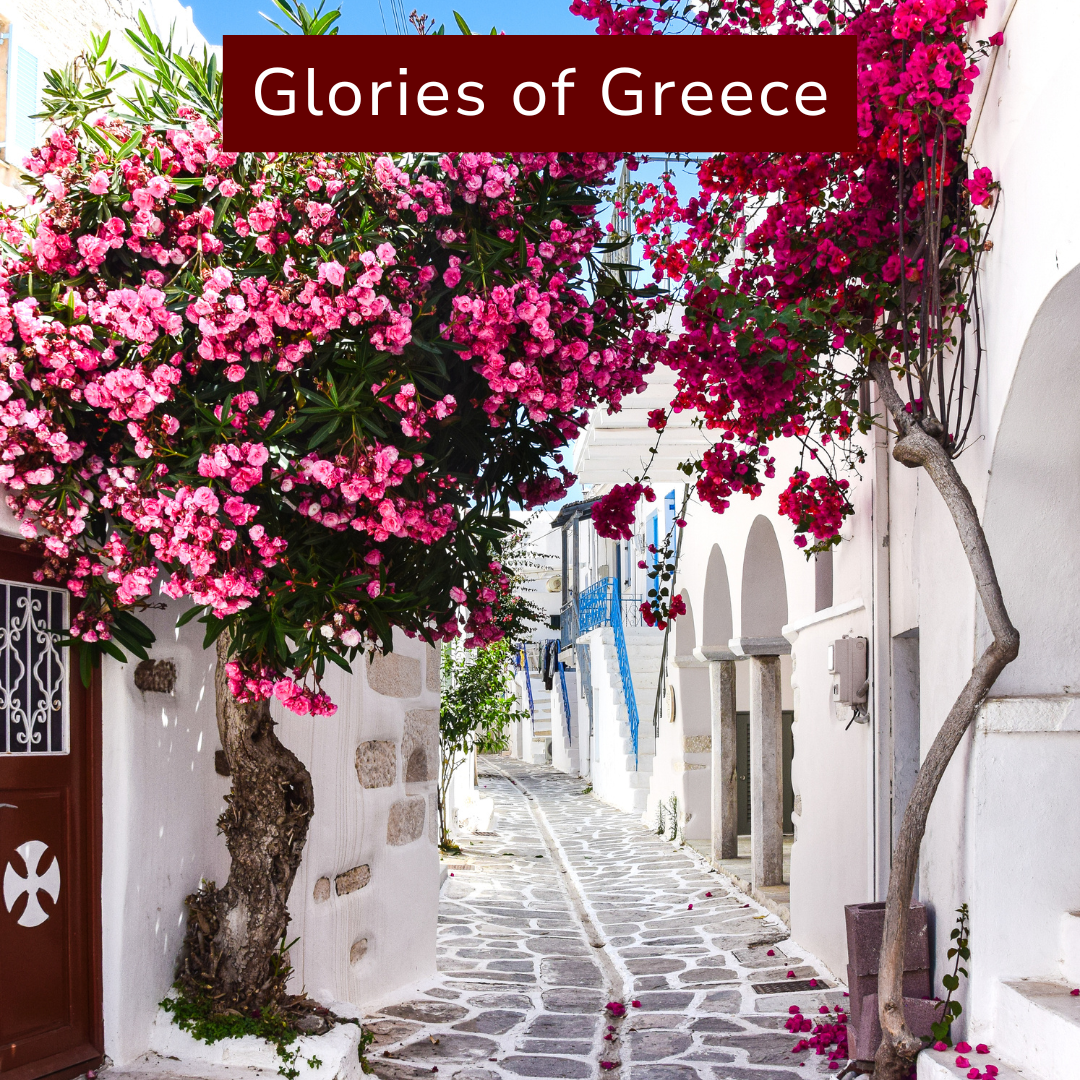 A narrow cobblestone street in Greece with white buildings, colorful flowers, pink bougainvillaea, and blue accents, under a clear blue sky.