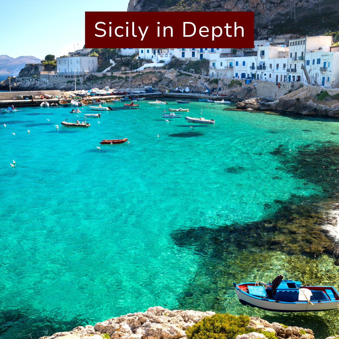 A panoramic view of a harbor in Sicily with turquoise water, several small boats floating, and white buildings with blue doors on a hillside in the background. The image has a banner with the text 'Sicily in Depth' at the top.