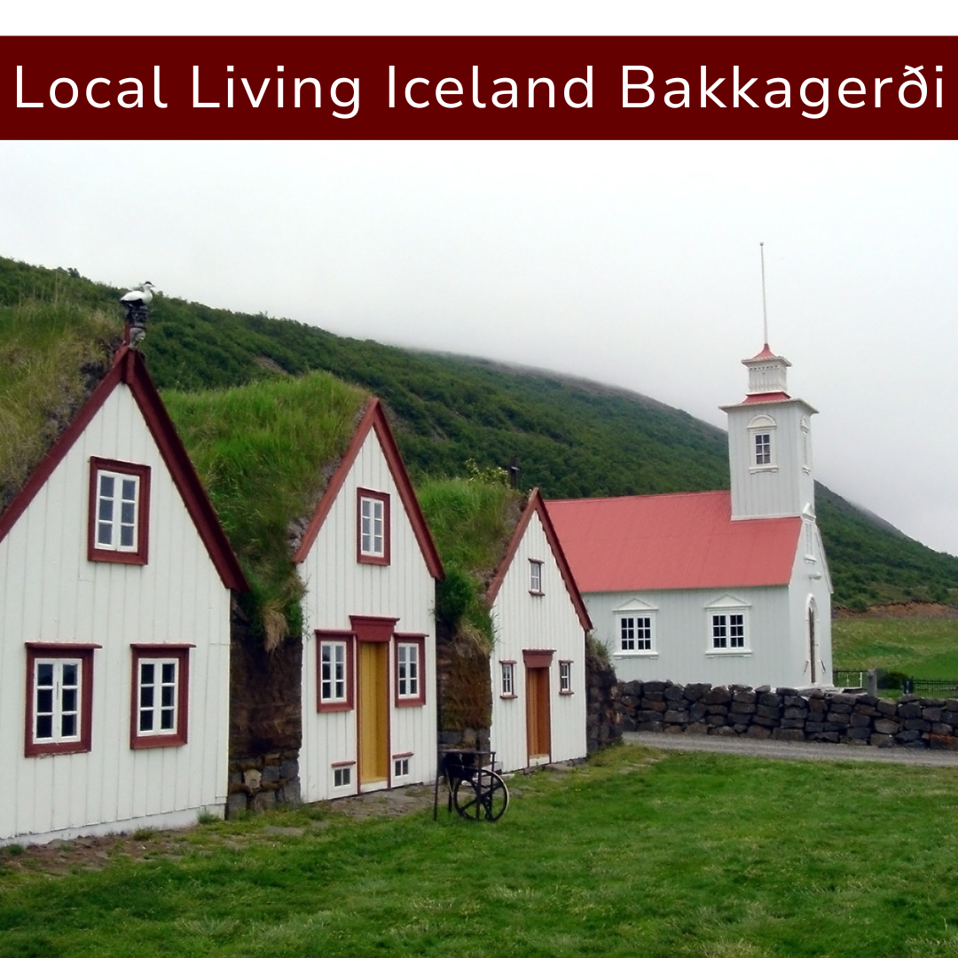 White Icelandic homes with red roofs and trim, a white church with a red roof, set against green hills and foggy sky.