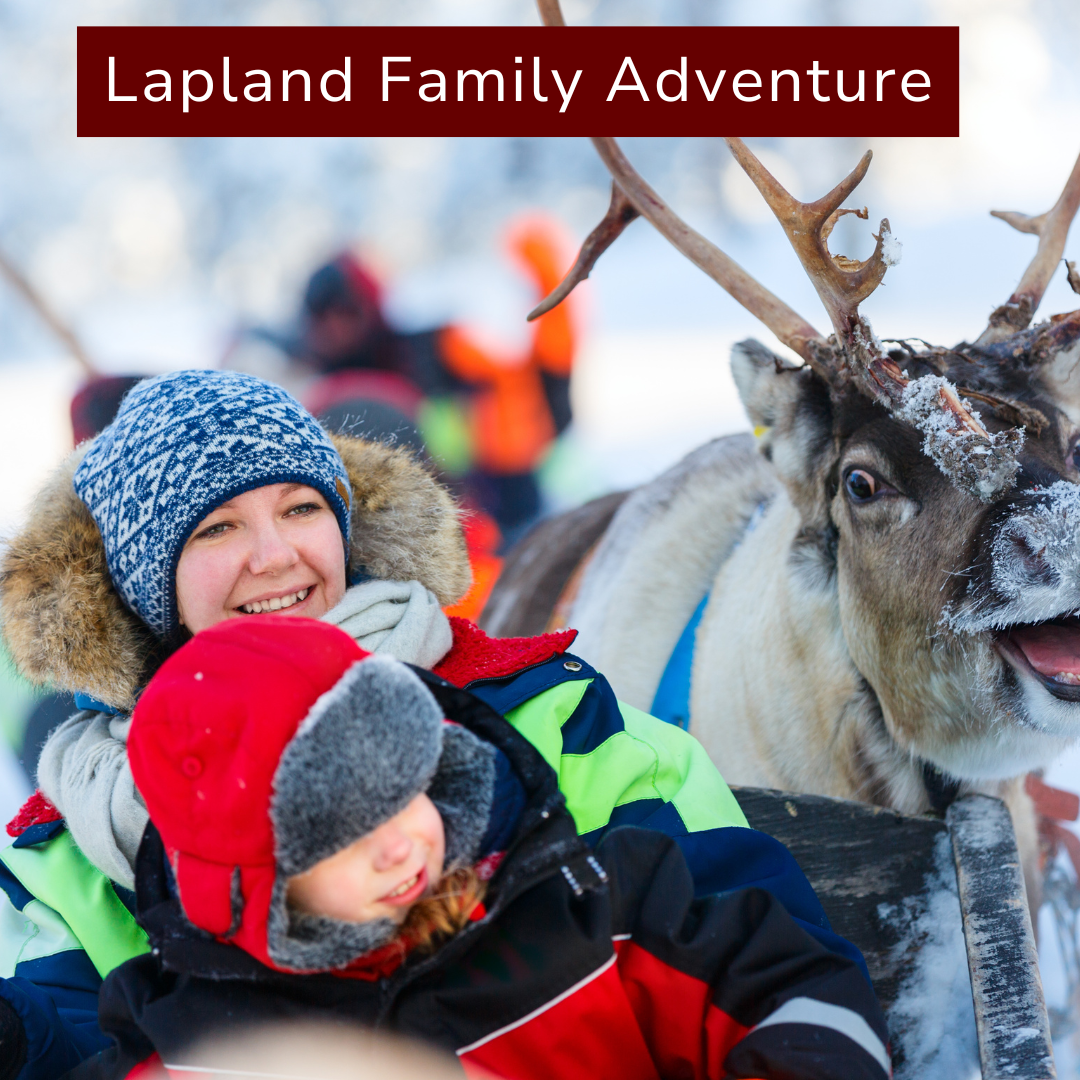 A smiling woman and a child bundled in winter clothing with a reindeer in a snowy outdoor setting, part of a Lapland family adventure.