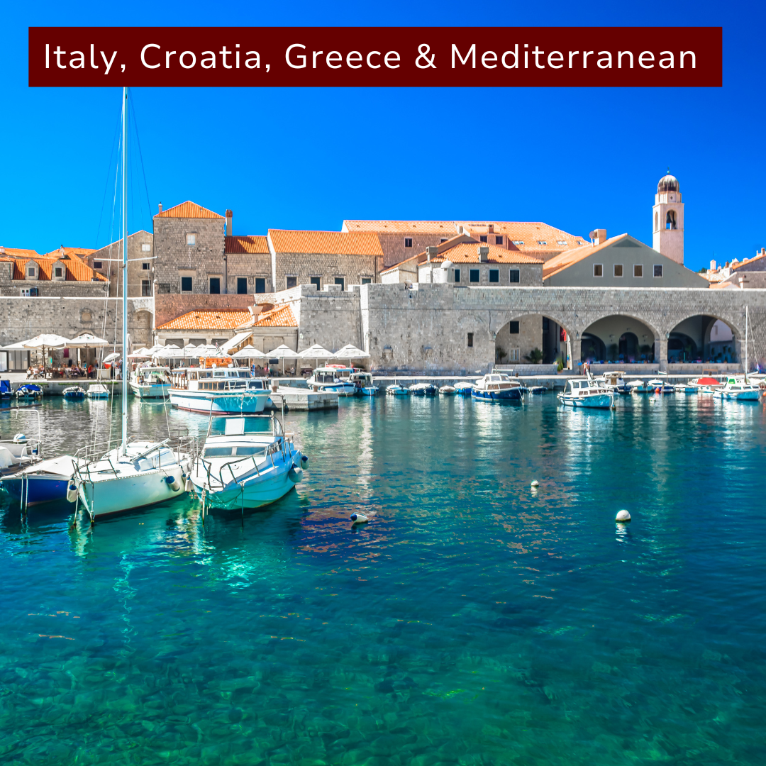 Harbor scene in Croatia with sailboats docked along clear blue water, historic stone buildings with orange rooftops, and a bright blue sky.