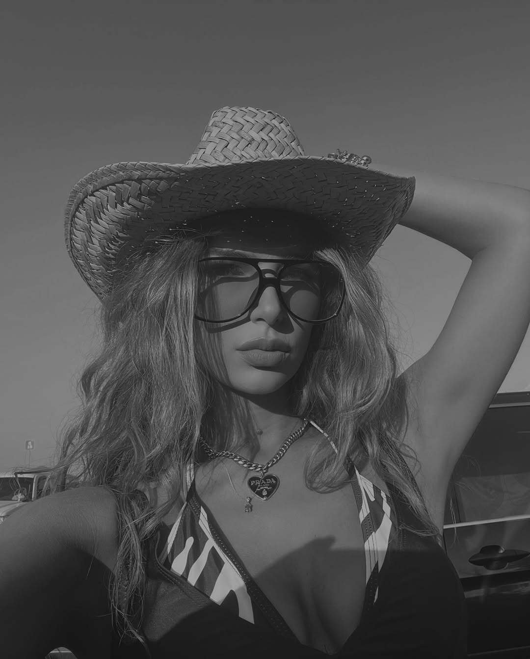 Black and white portrait of a woman wearing a straw cowboy hat, oversized sunglasses, and a sporty bikini-style top at a summer music festival.