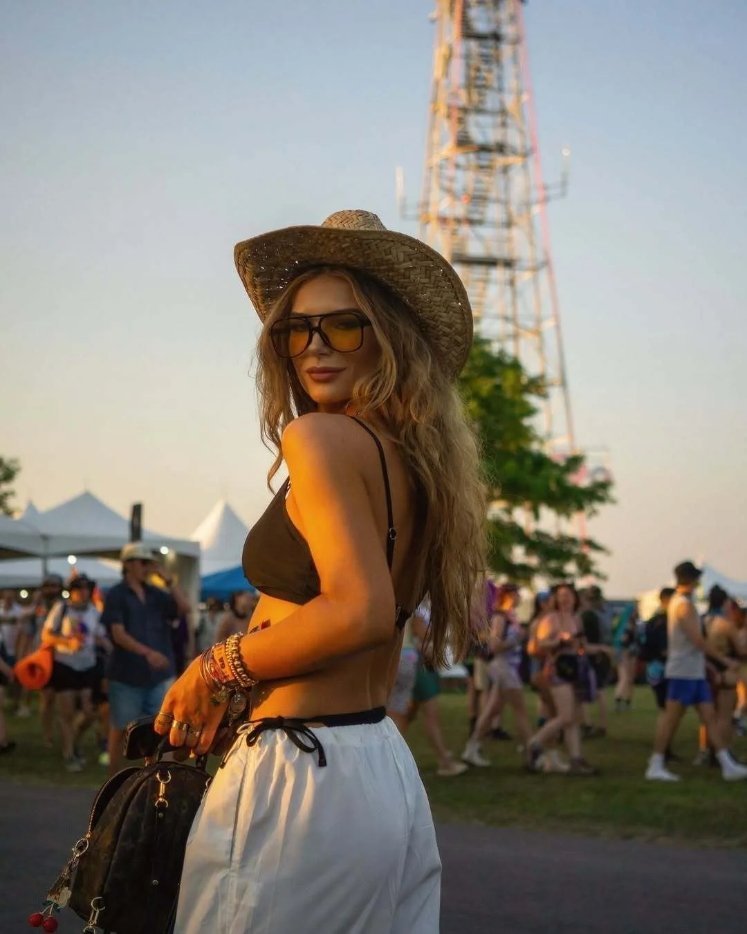 Woman wearing white lightweight parachute pants and a black bikini top at Bonnaroo with a Ferris wheel in the background at sunset.