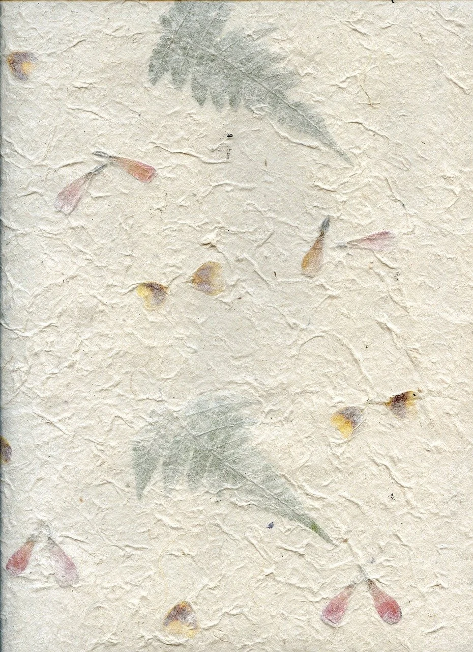 A textured, cream-colored paper with faded green leaves and pink, purple, and yellow flower petals scattered across it.