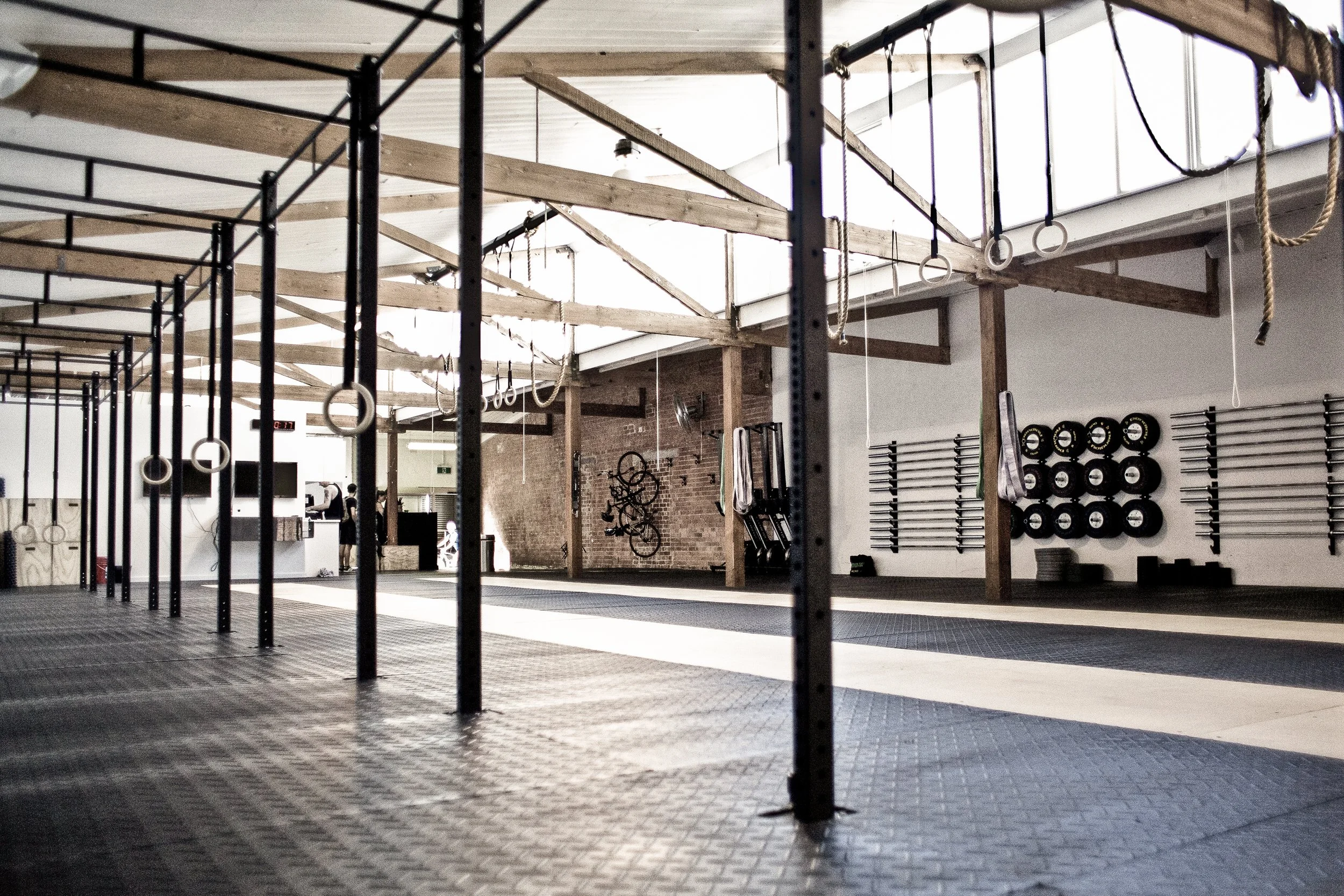 Empty CrossFit gym with pull-up bars, rings, weights, and ropes, featuring wooden ceiling beams.