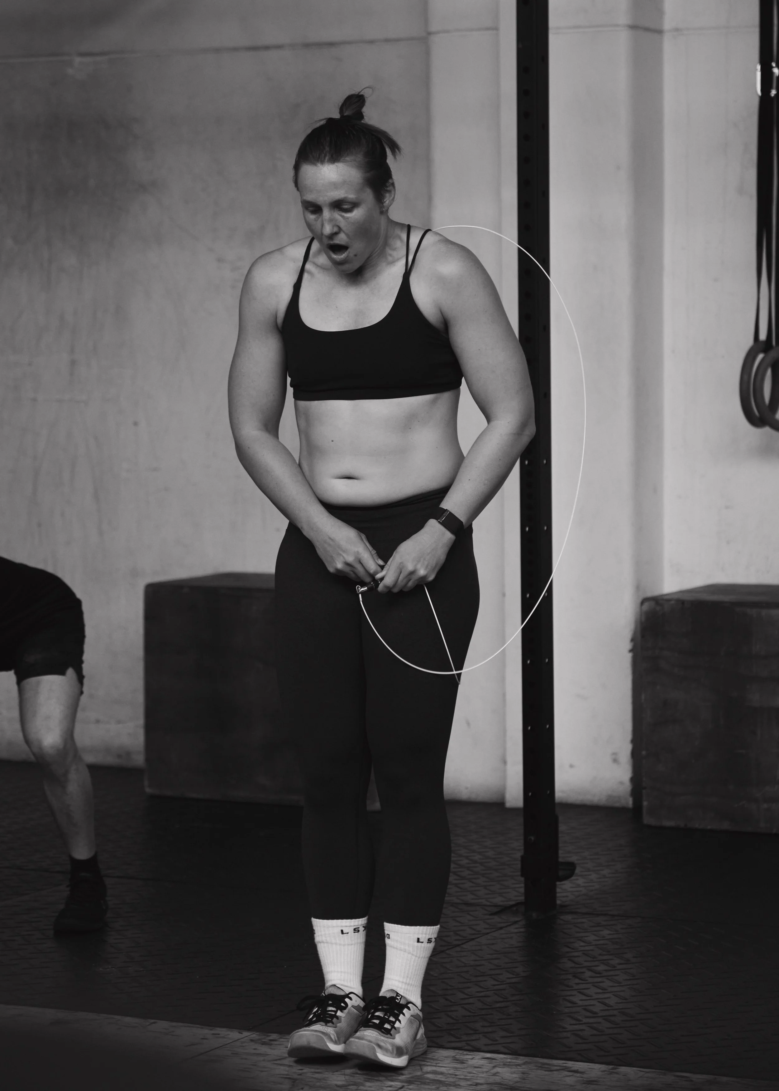 Person in a gym holding a jump rope, wearing athletic clothing, looking tired.
