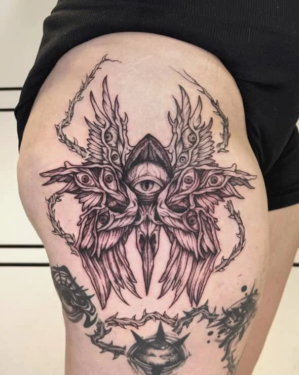Tattoo of a symmetrical moth with an eye in the center of its forehead and intricate wing details, surrounded by abstract designs.