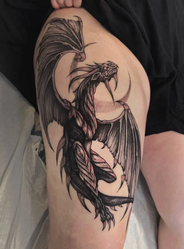 Black and gray tattoo of a dragon on a person's thigh.