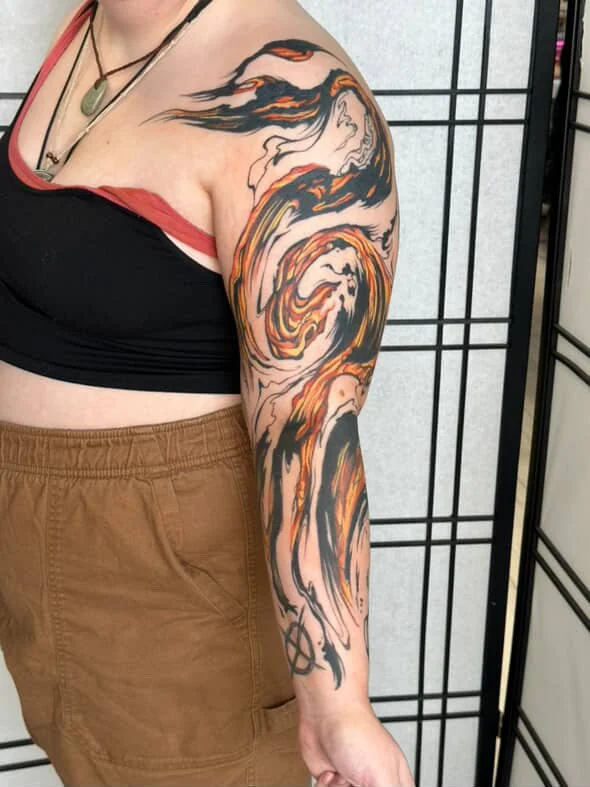 A person with a colorful, swirling tattoo on their upper arm and shoulder, featuring abstract flames in black, orange, and yellow tones.
