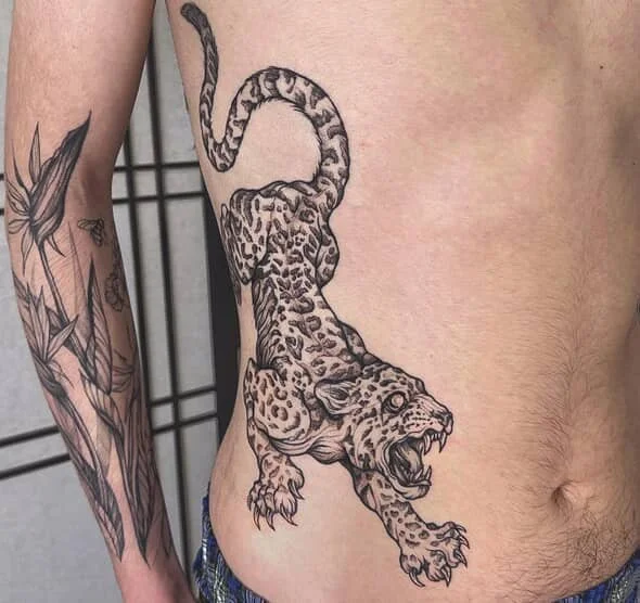 Tattoo of a crouching, roaring leopard on a person's side and torso.