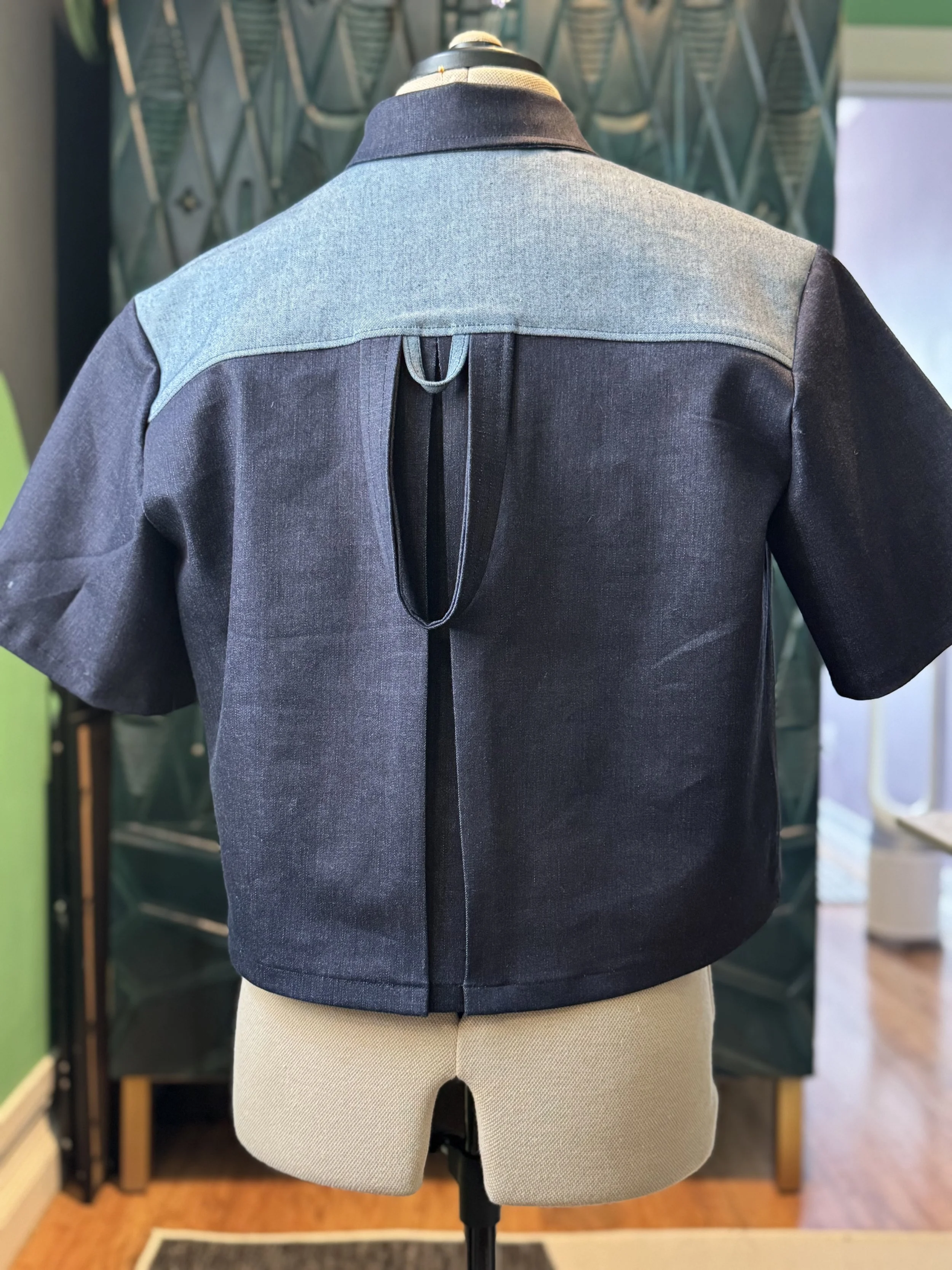 A mannequin wearing a jacket with a light blue yoke and dark gray sleeves, and beige pants, displayed in a clothing store.