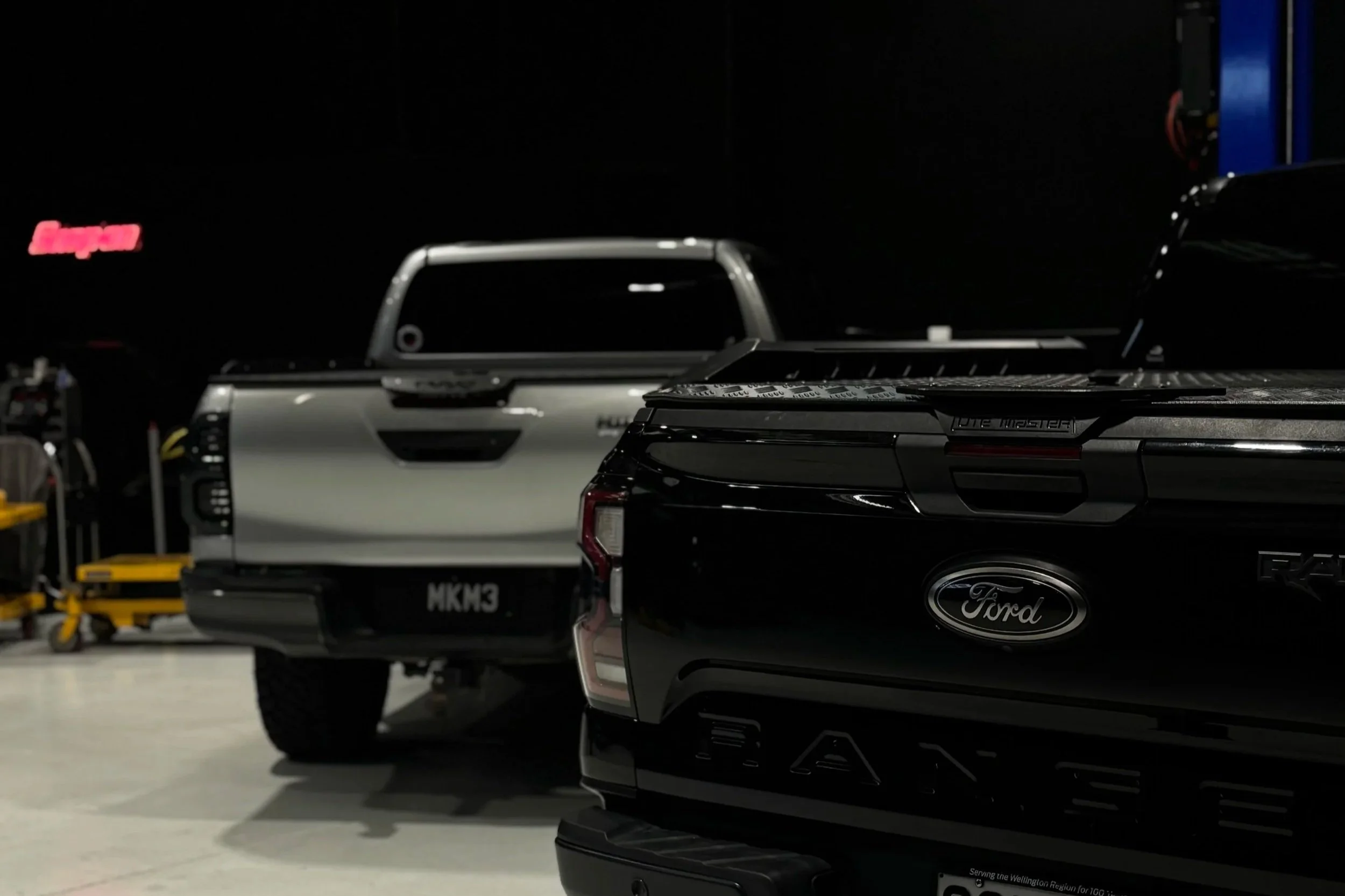 Black Ford Ranger pickup truck and silver Toyota Hilux pickup truck parked in a garage.