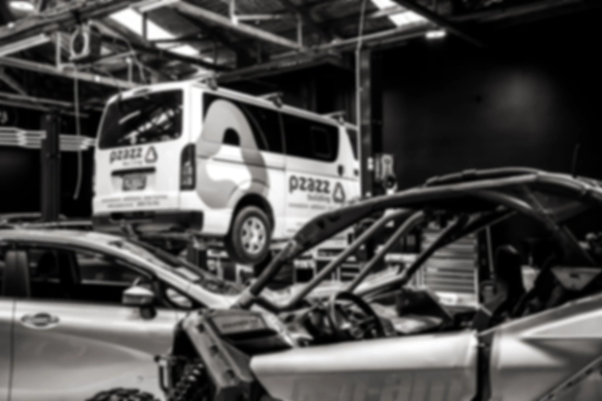 White van on a hydraulic lift in an auto repair shop, with logos and text for 'PERSONNEL TOUCH' and contact number, and a technician working nearby.