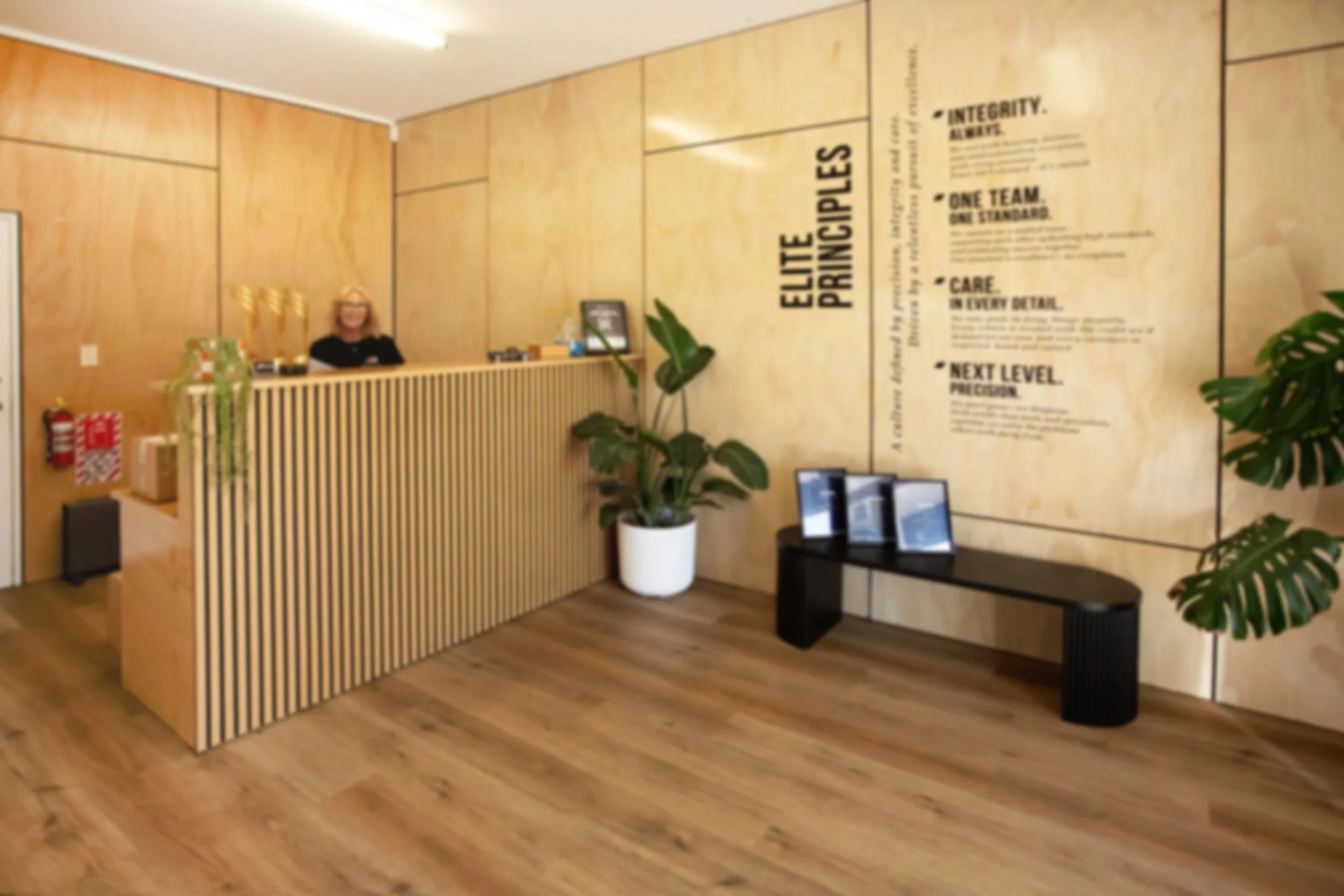 Two mechanics working in a garage with a large sign that reads 'Elite Diagnostics' on the back wall and a white vehicle partially visible on the left.