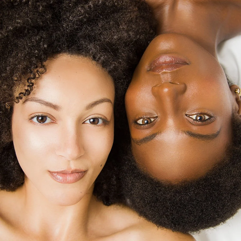 Two women with natural curly hair lying down, facing upwards, close together.