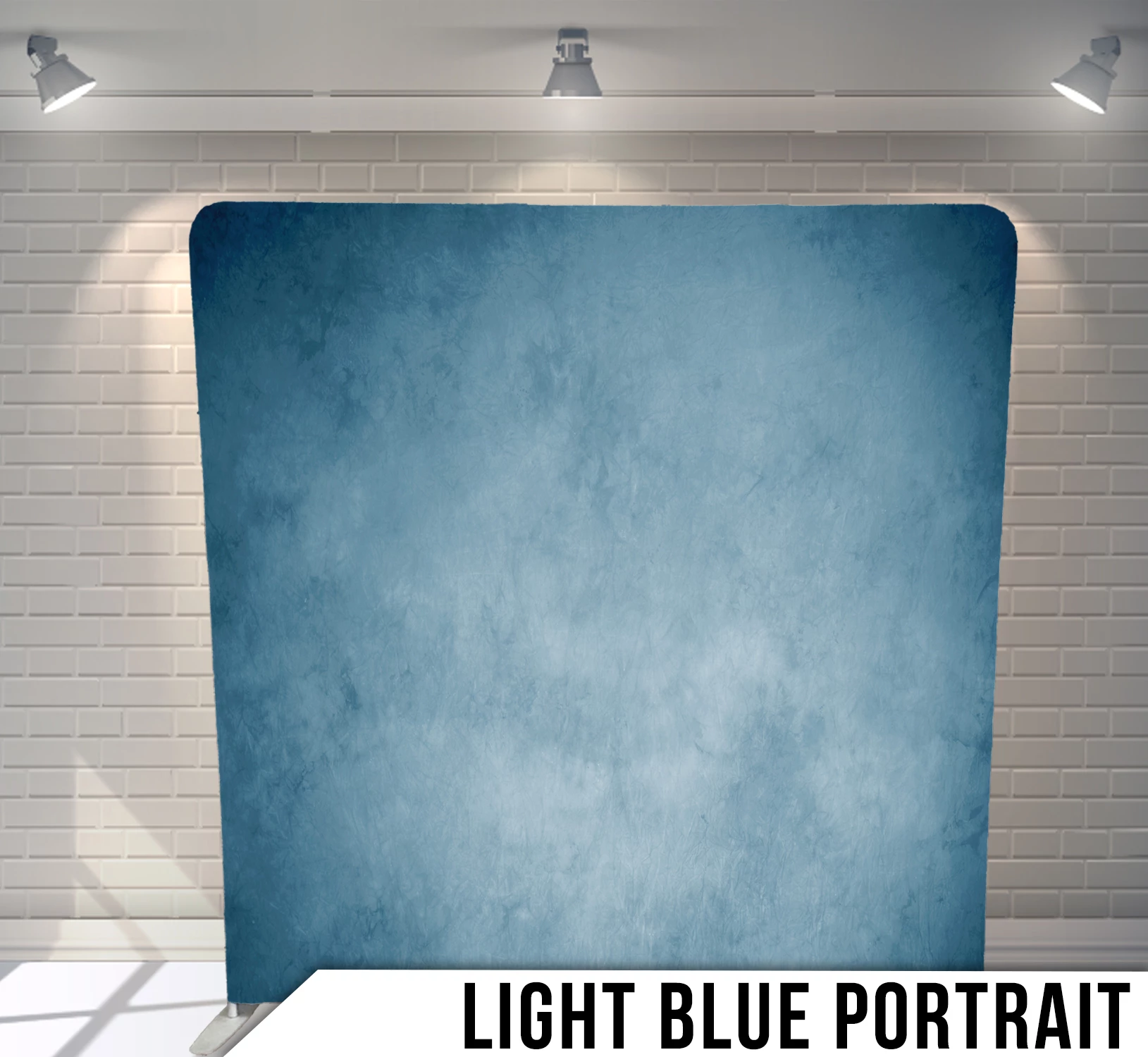 Light blue textured portrait backdrop in a room with white brick walls and overhead lighting.