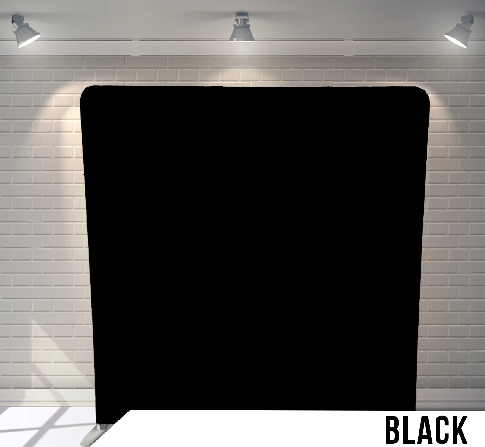 Black backdrop in front of a white brick wall with spotlights overhead.