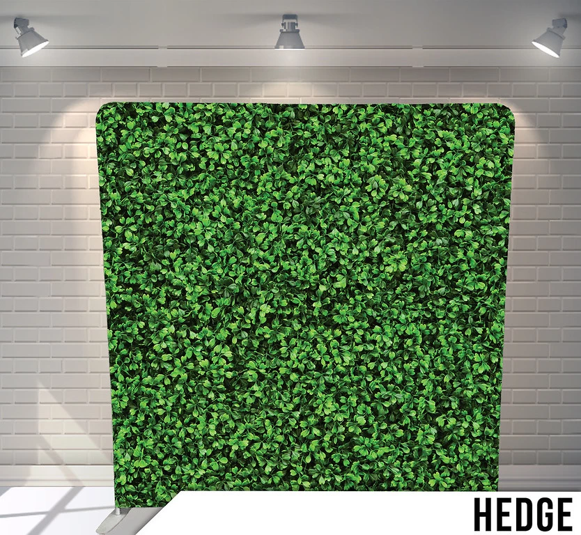 Artificial hedge panel displayed indoors with spotlights, brick wall background.