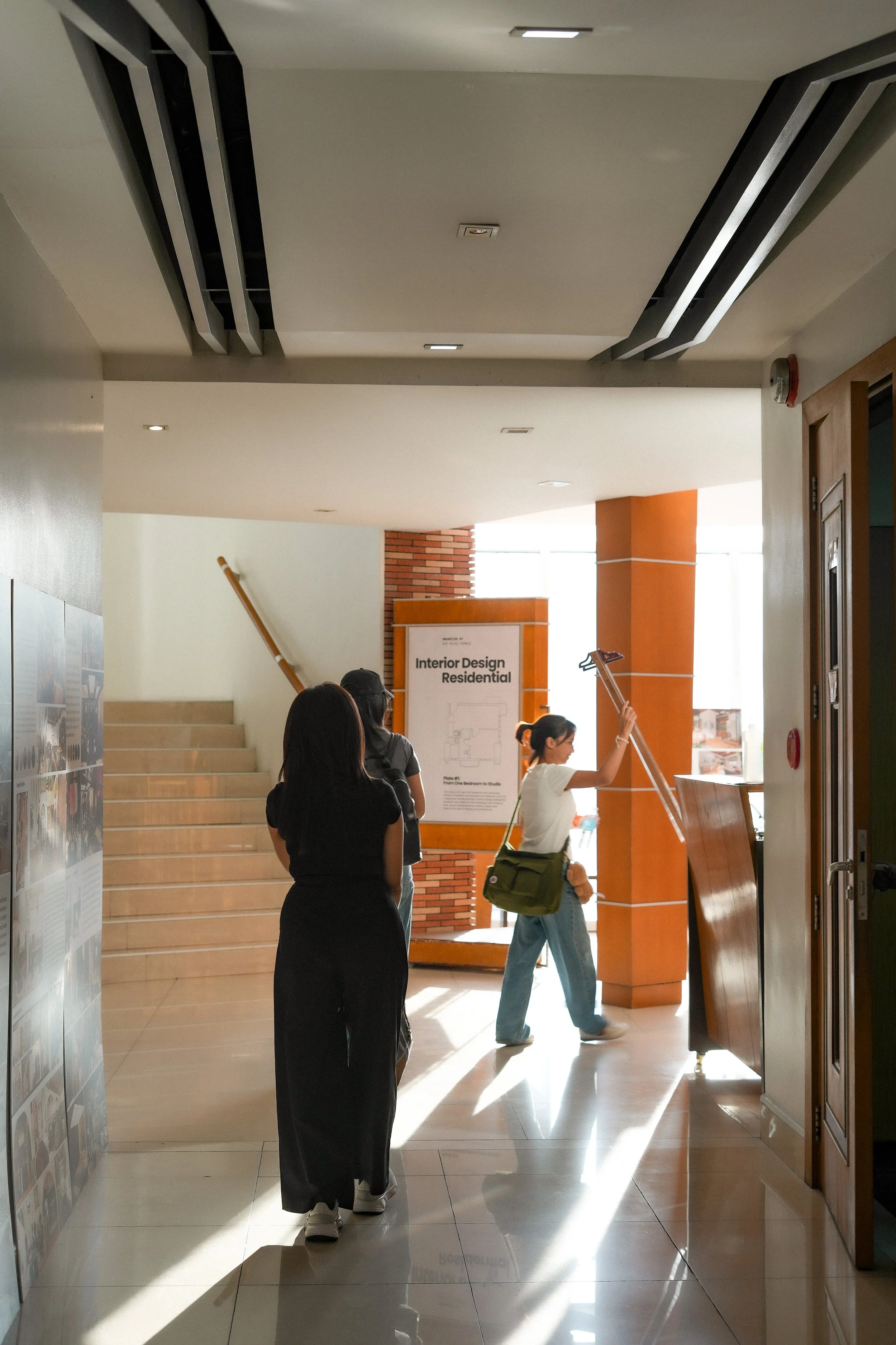 People walking in a corridor with steps, a sign for interior design, and sunlight coming through the windows.