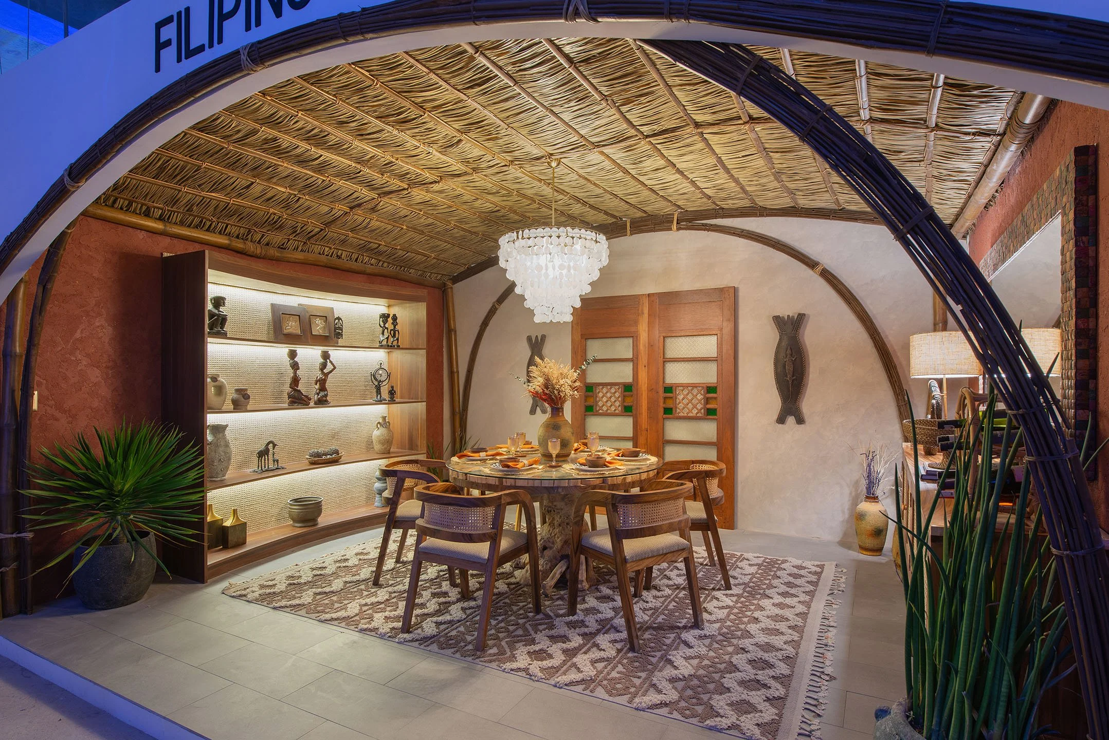 Interior of a tropical-themed dining room with a bamboo ceiling, a chandelier, a round dining table with chairs, and decorative art pieces on the wall.