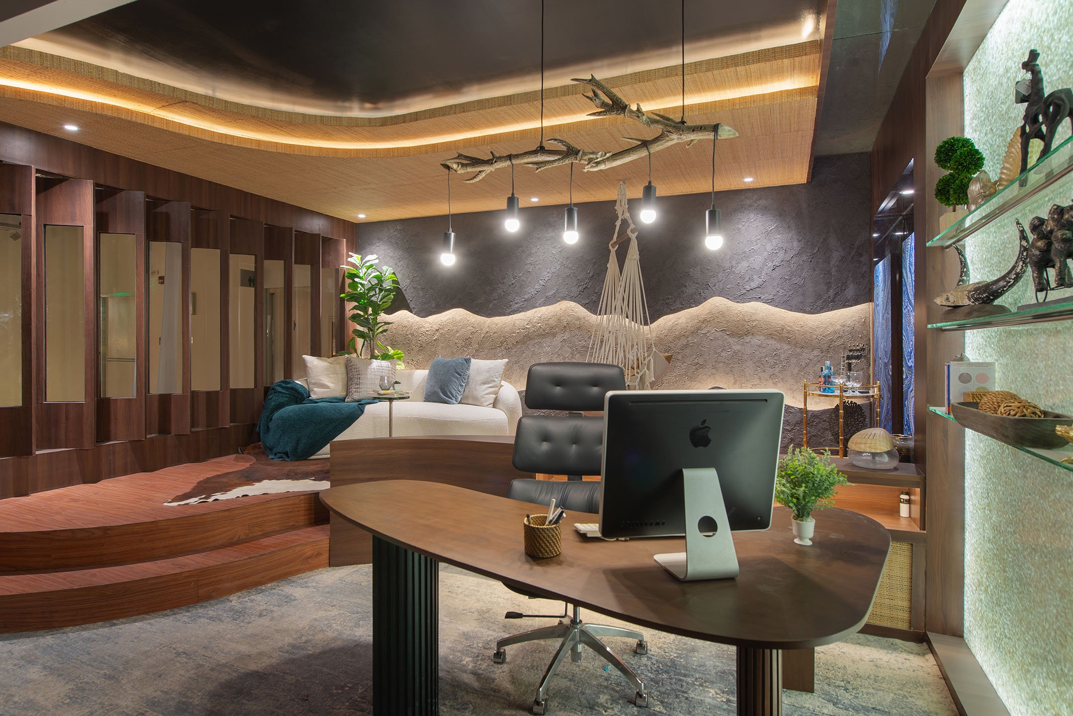 Modern home interior with a wooden ceiling, hanging branch fixture, a bench with pillows, green plants, and decorative shelves with artwork and sculpture.