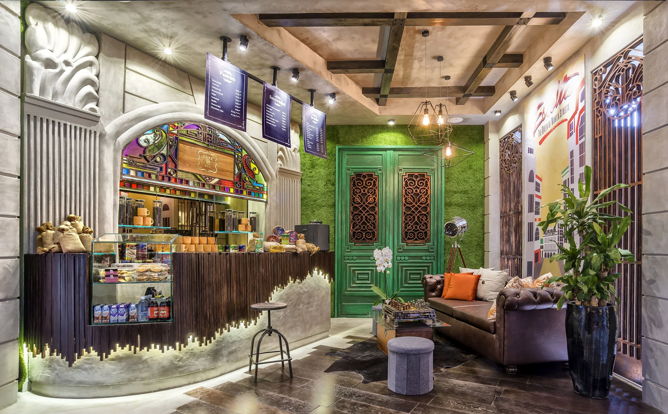 Interior of a cozy cafe with a decorative counter, green doors, a mural of buildings, and a seating area with a brown leather sofa and orange pillows, illuminated by warm lighting.
