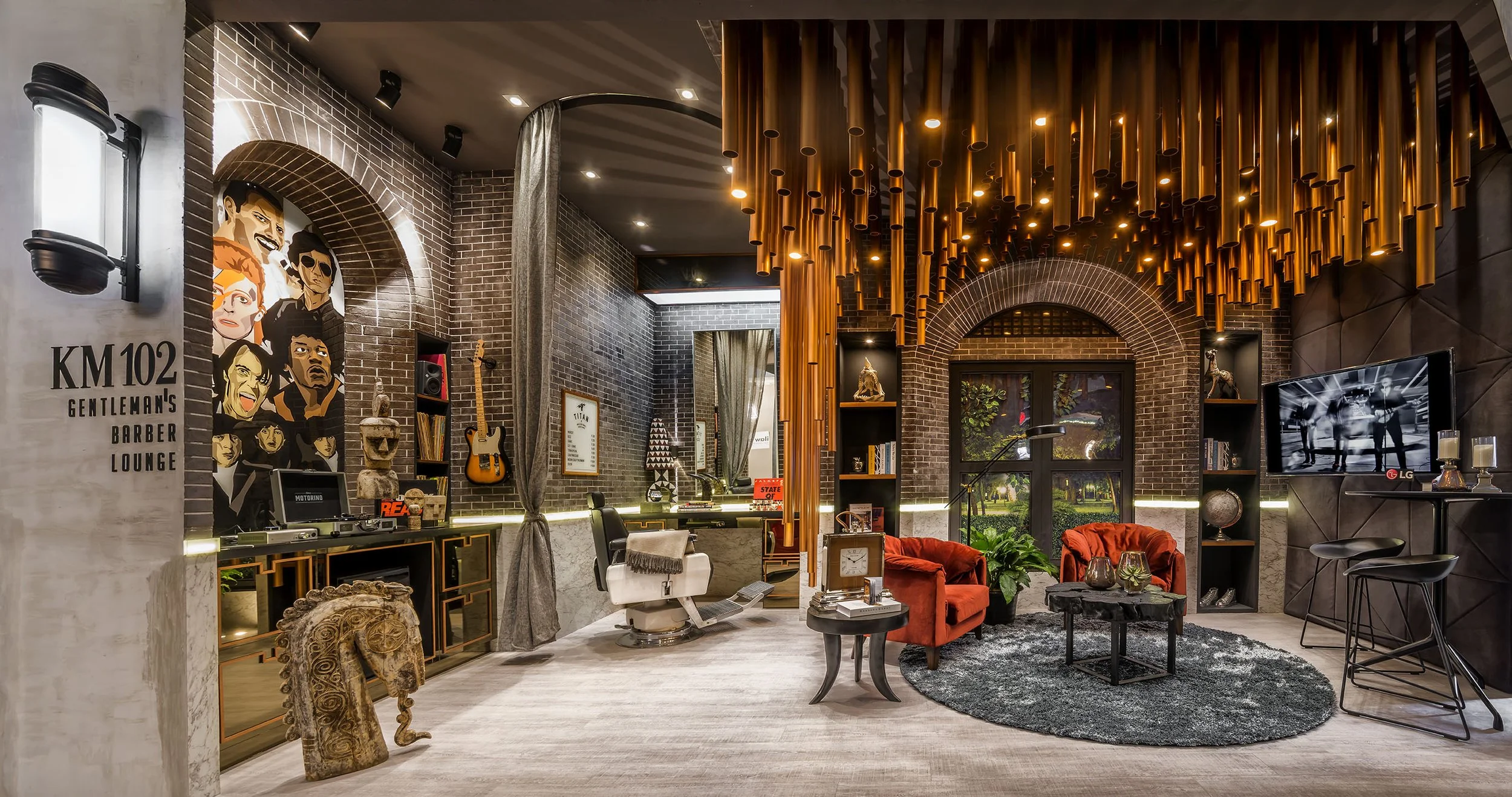 Modern interior of a lounge with brick walls, decorative items, a mounted guitar, a TV, and plush chairs, with a striking copper pipe ceiling design.